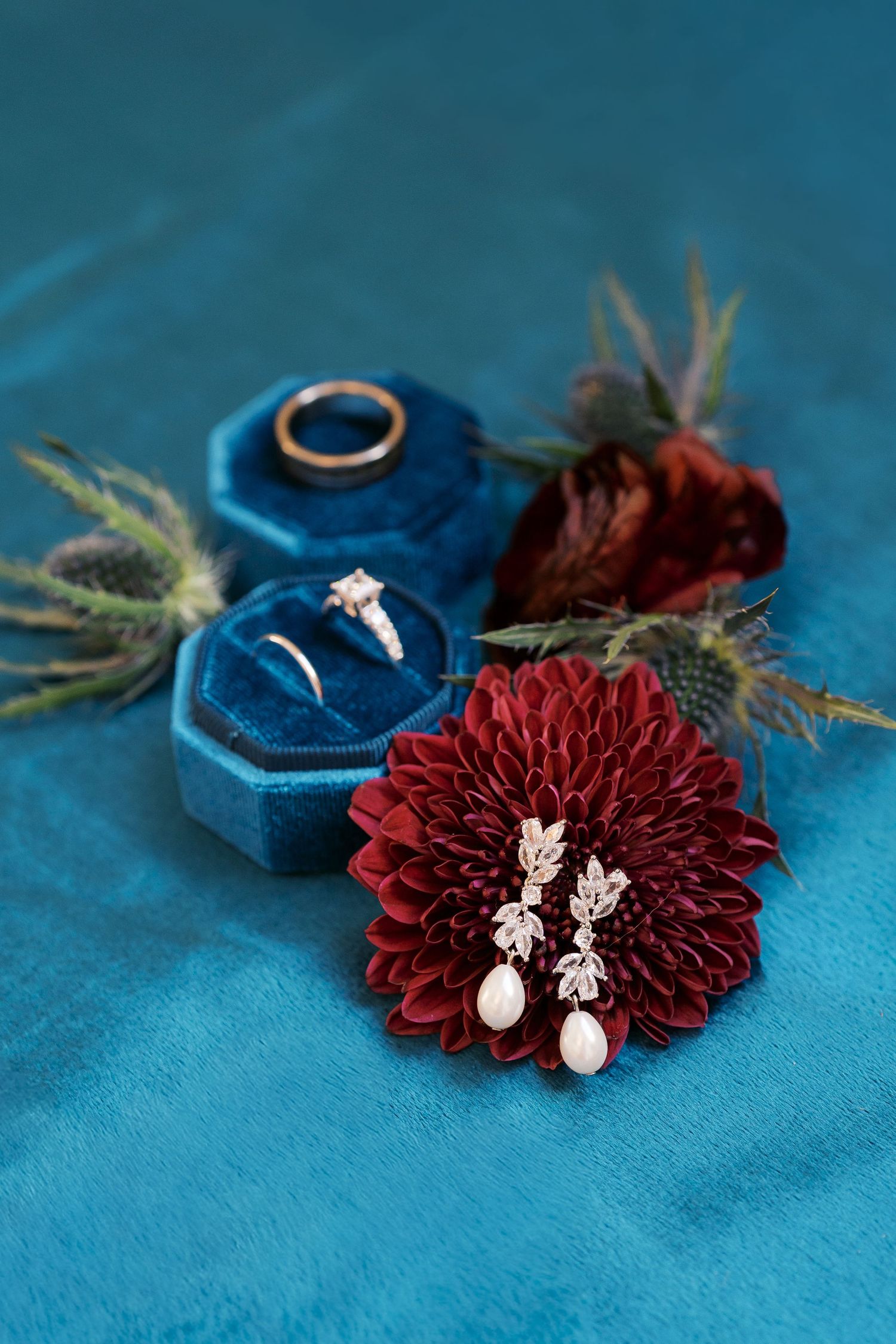 Wedding jewelry and burgundy flowers arranged on rich blue velvet surface.