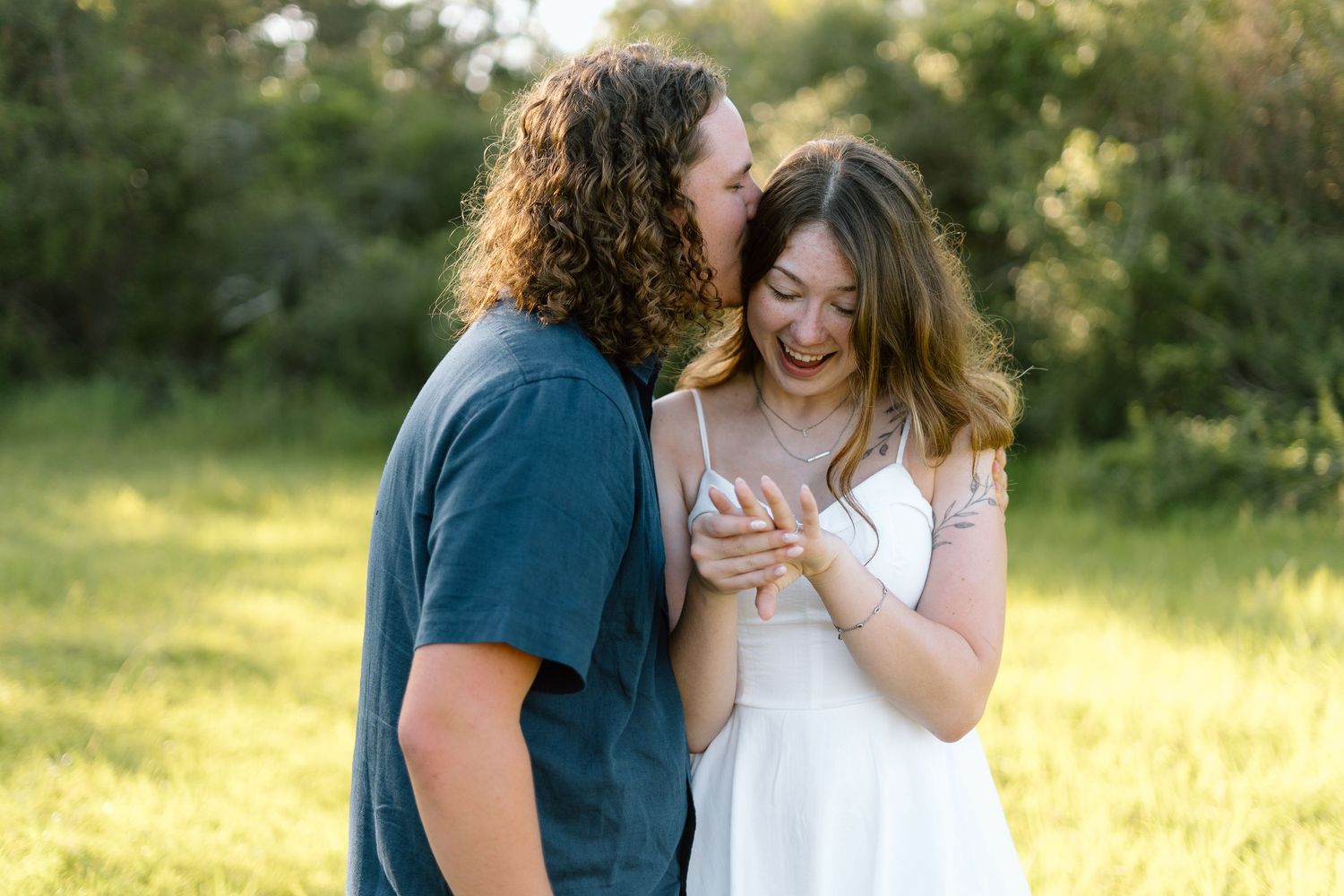 Couple embracing in a sunny meadow with golden light filtering through trees.