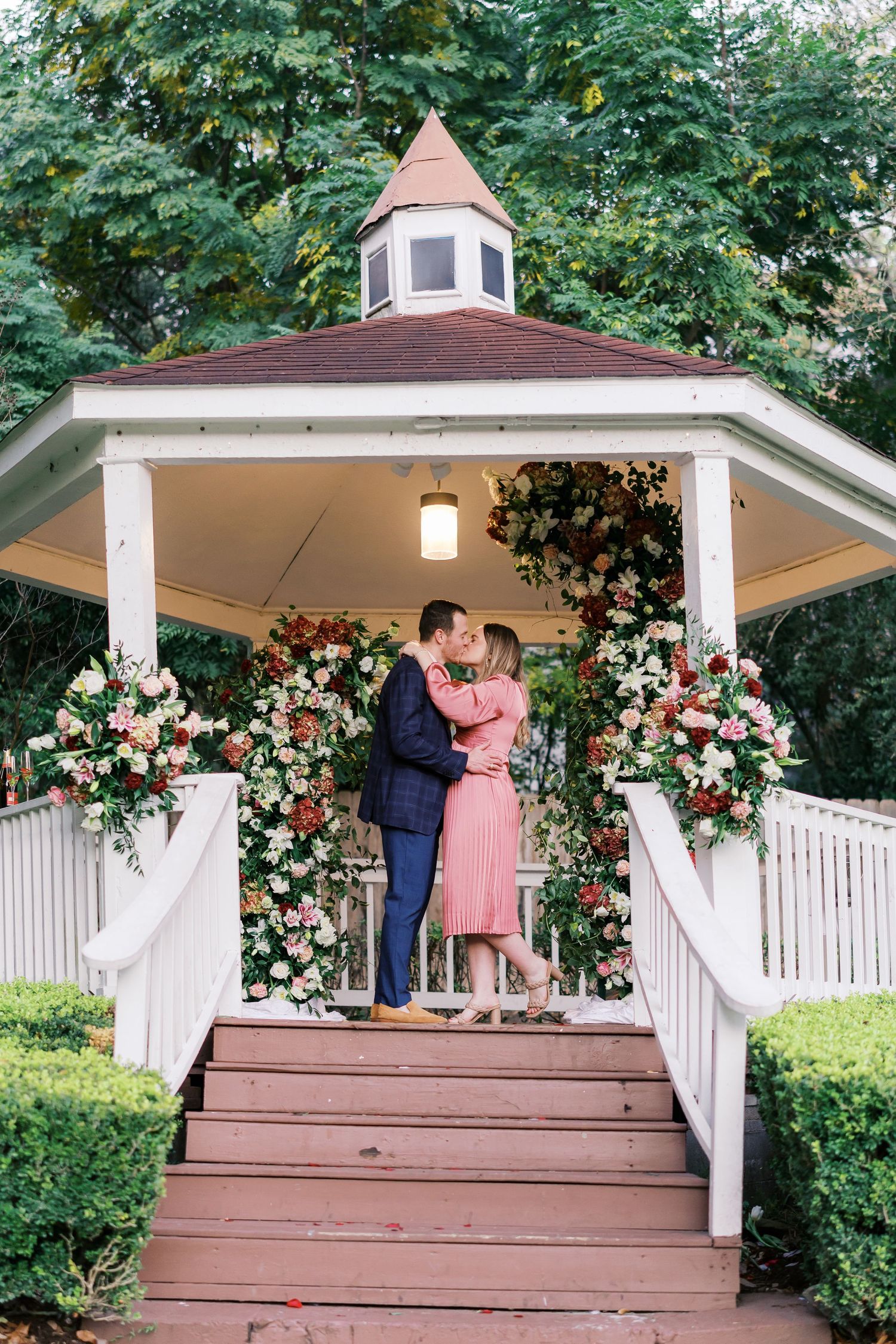 White gazebo decorated with floral arrangements sets the scene for a romantic proposal.