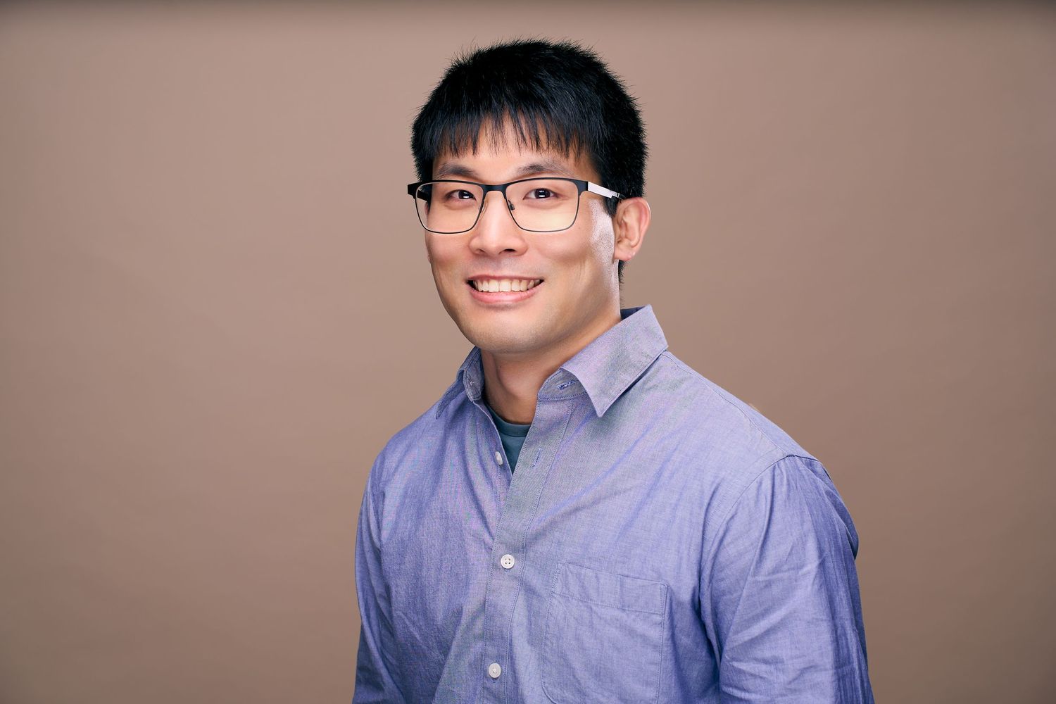 Professional headshots of someone wearing glasses and a light blue button-down shirt against a neutral background.
