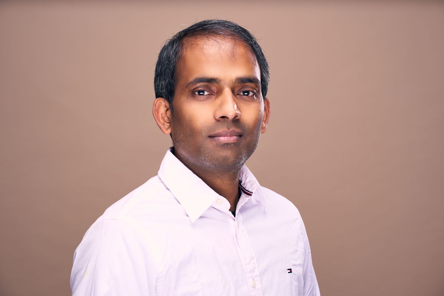 Professional headshot of person wearing a white button-down shirt against a neutral background.