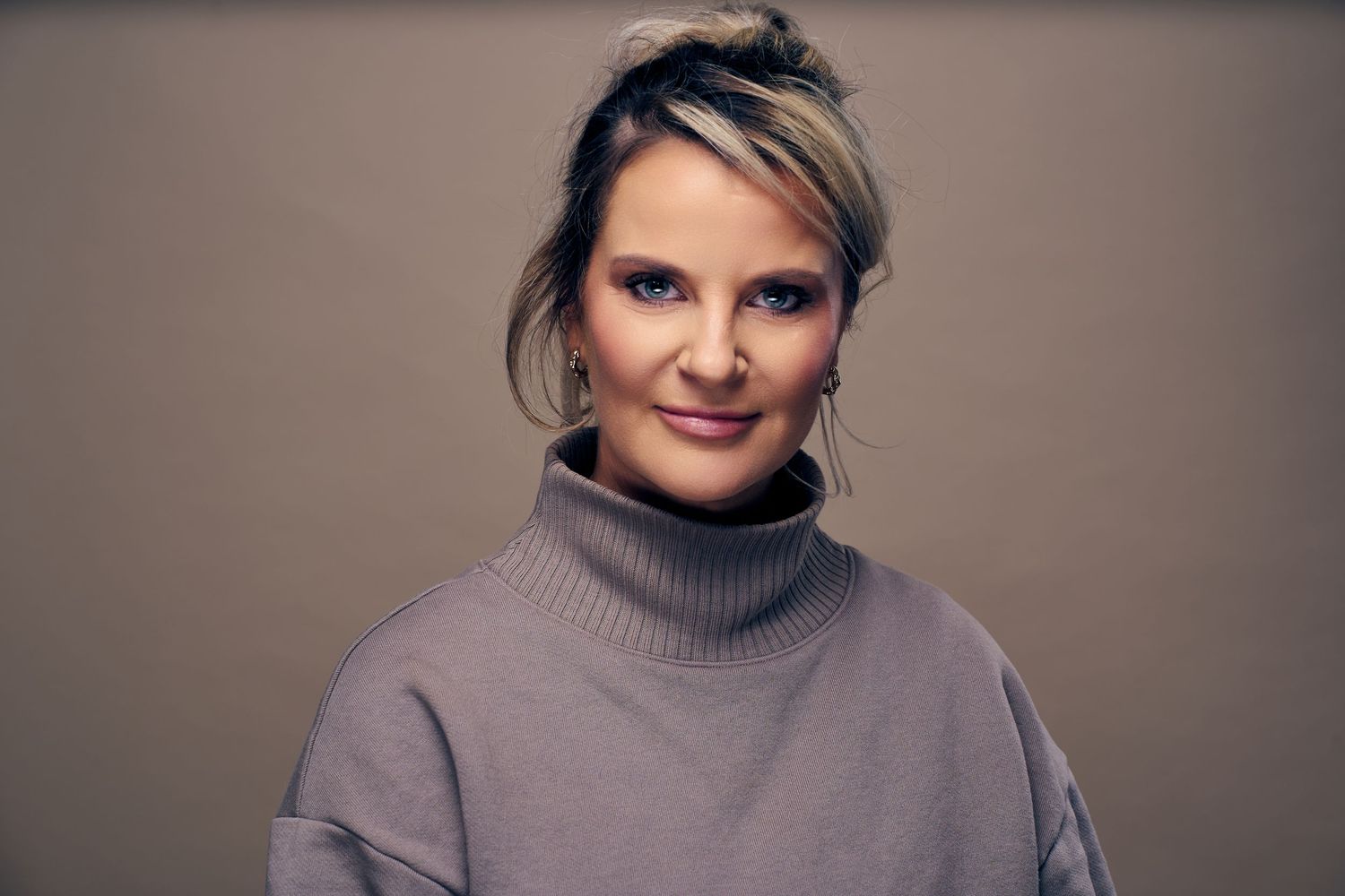 Professional studio portrait of someone wearing a gray turtleneck sweater against a neutral background.