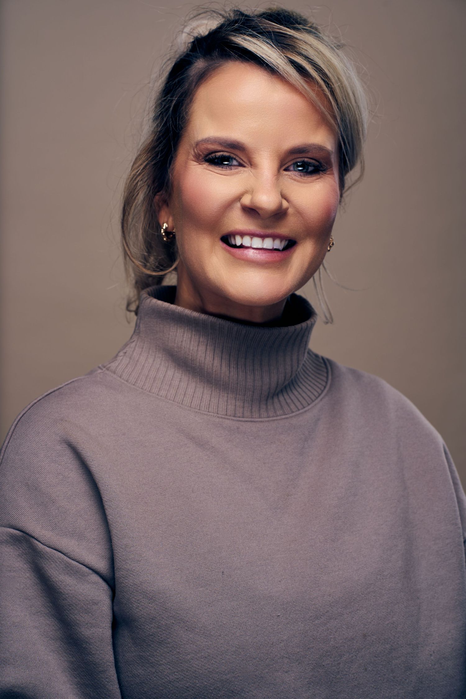 A person in a gray turtleneck sweater smiles warmly in a series of connected portrait photos.