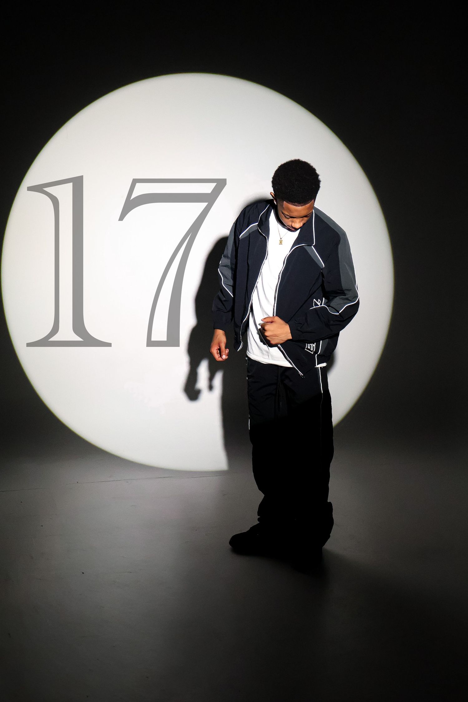 Man in dark jacket posing against illuminated circle backdrop with number 17 in a dramatic studio setting.