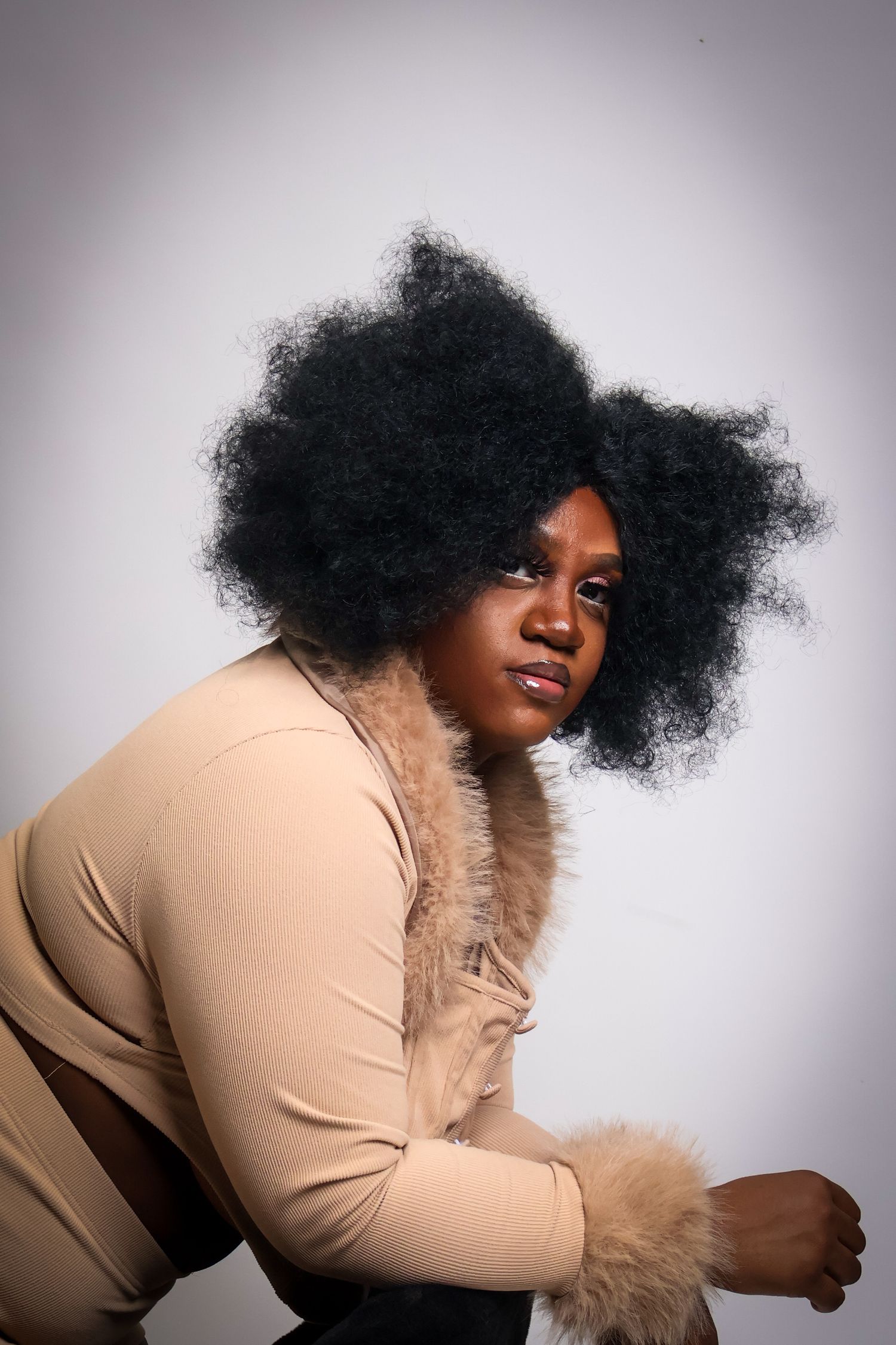 Woman with large natural afro hair wearing beige ribbed outfit with fur trim, side profile pose.