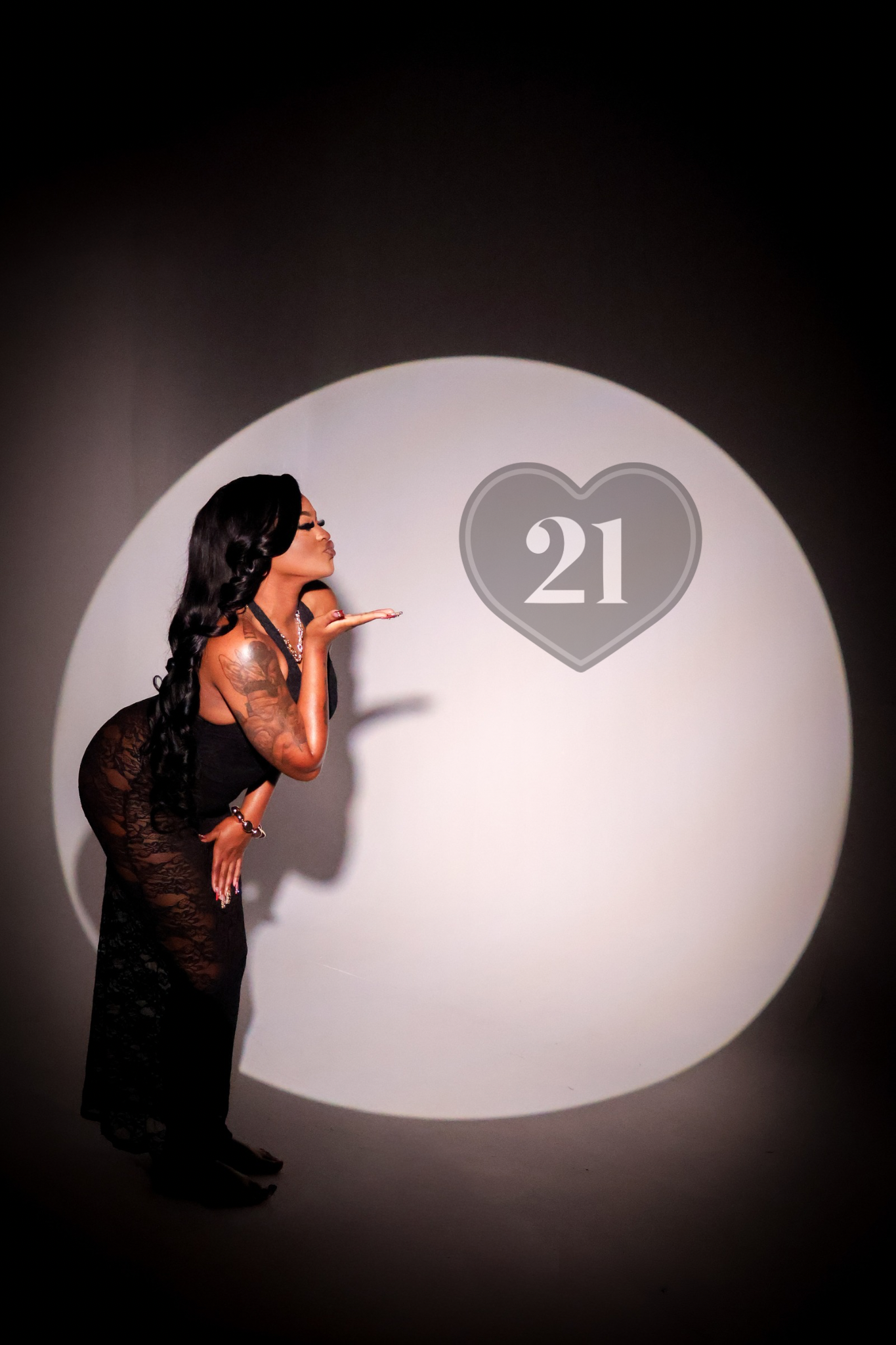 Woman in black outfit blowing a kiss toward a heart with number 21 in a spotlight circle.