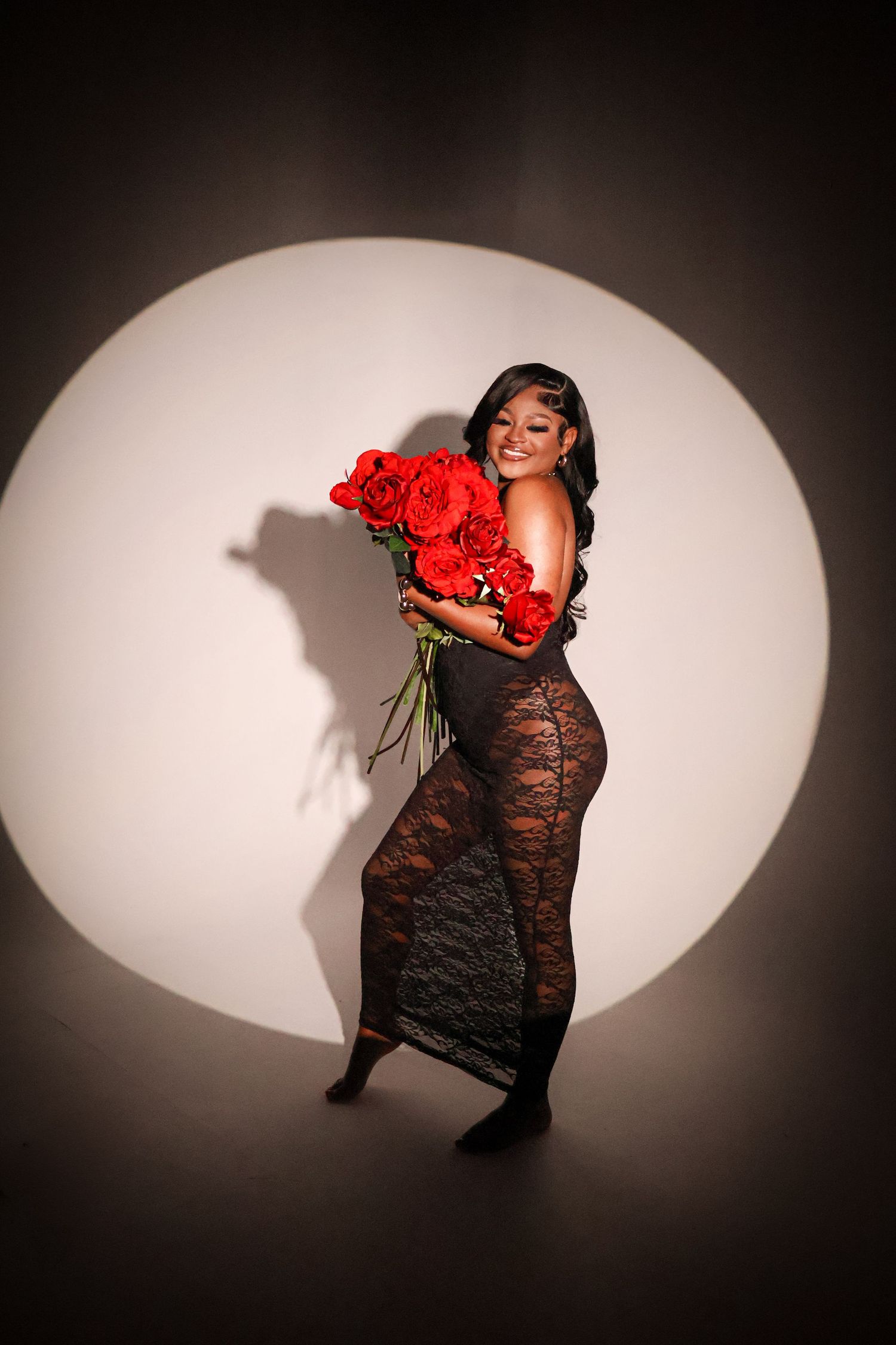 Woman in black lace dress holding large bouquet of red roses under spotlight.
