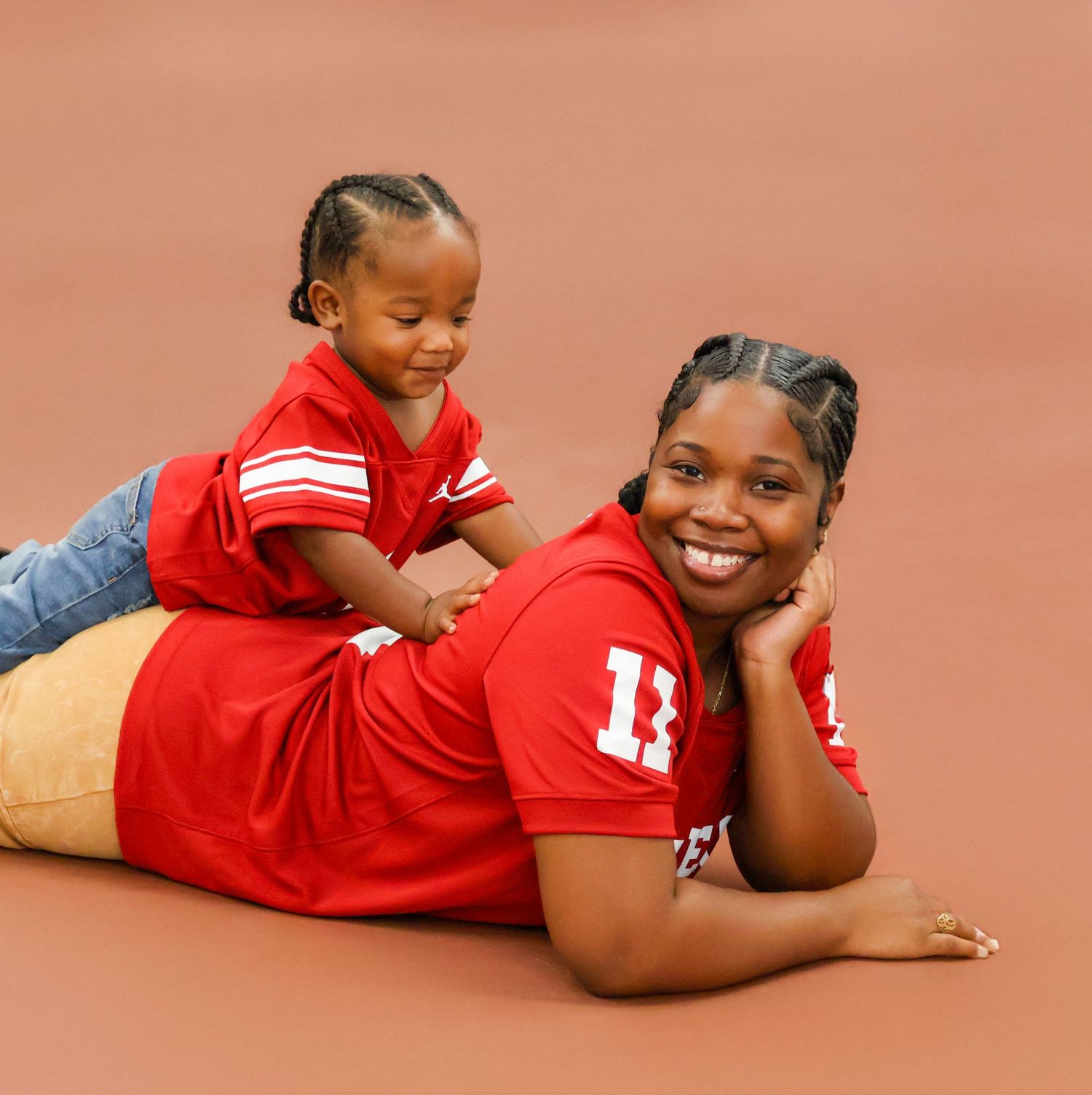 Woman and toddler in matching red football jerseys posing on court floor.