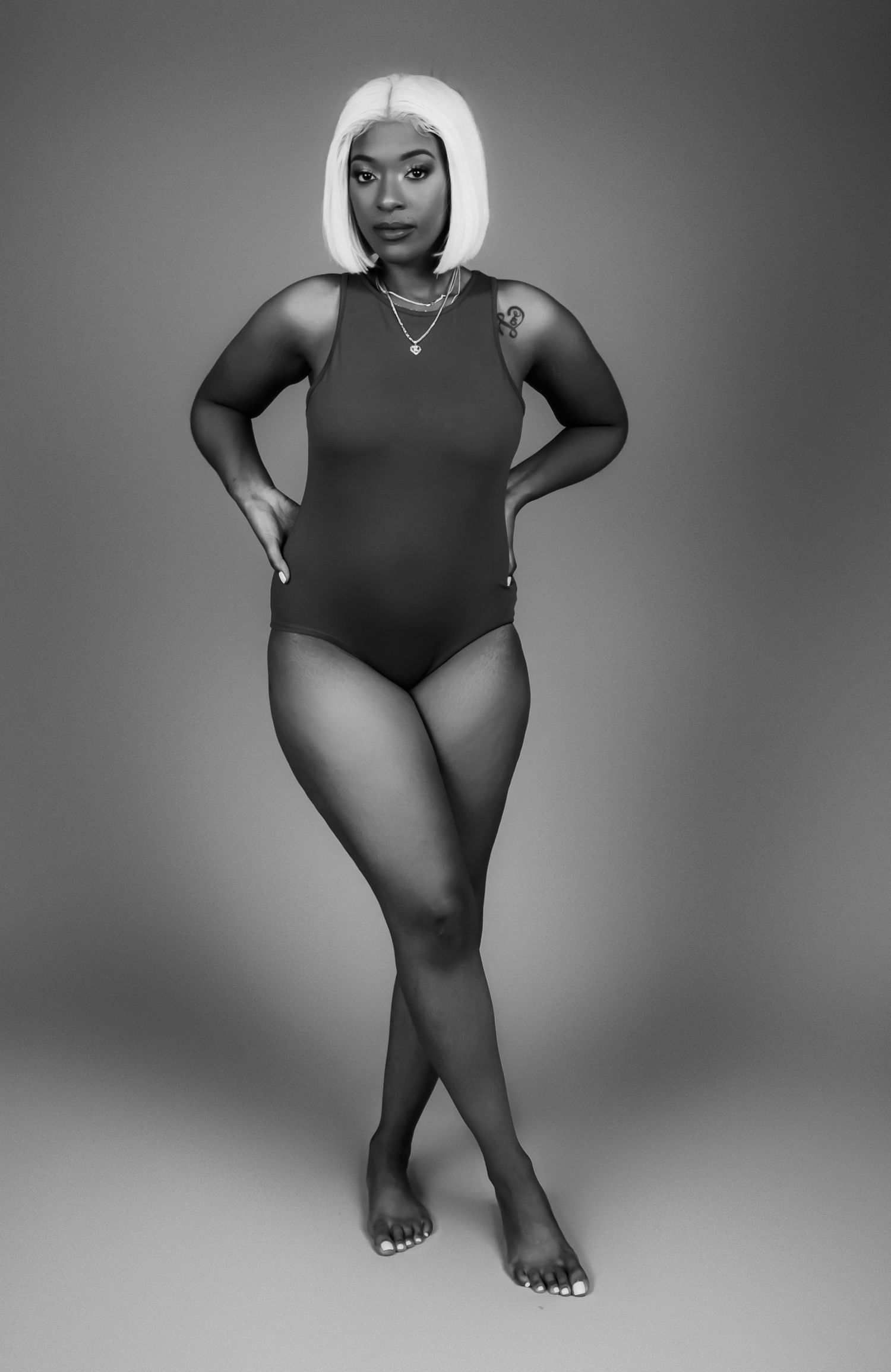 Black and white full body portrait of woman in bodysuit with blonde bob hairstyle.