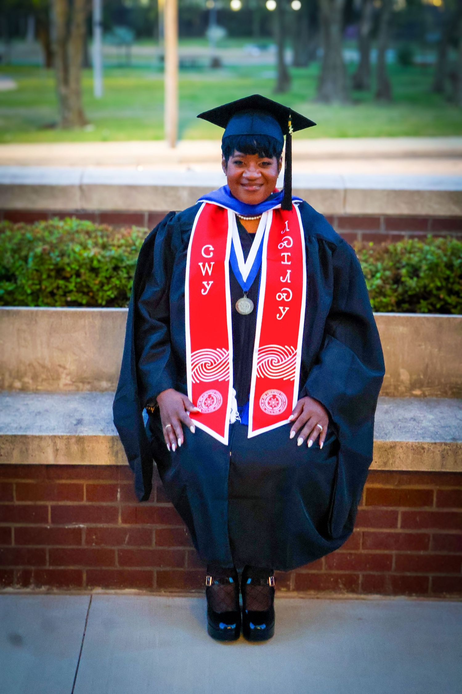 Proud graduate in black cap and gown with red CWY honor stole poses outdoors.