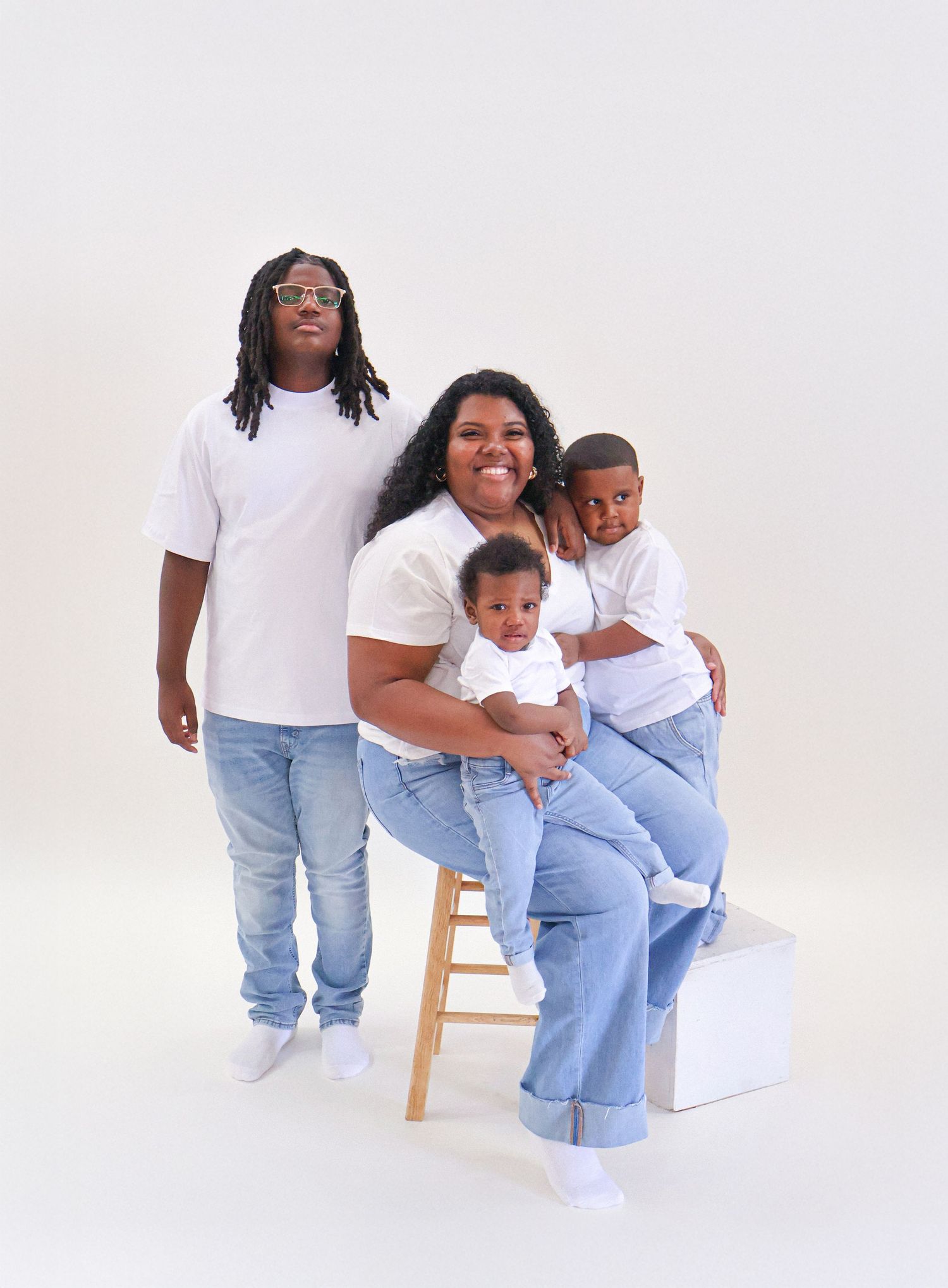 A smiling family of four in matching white tees and jeans poses together in a bright studio setting.