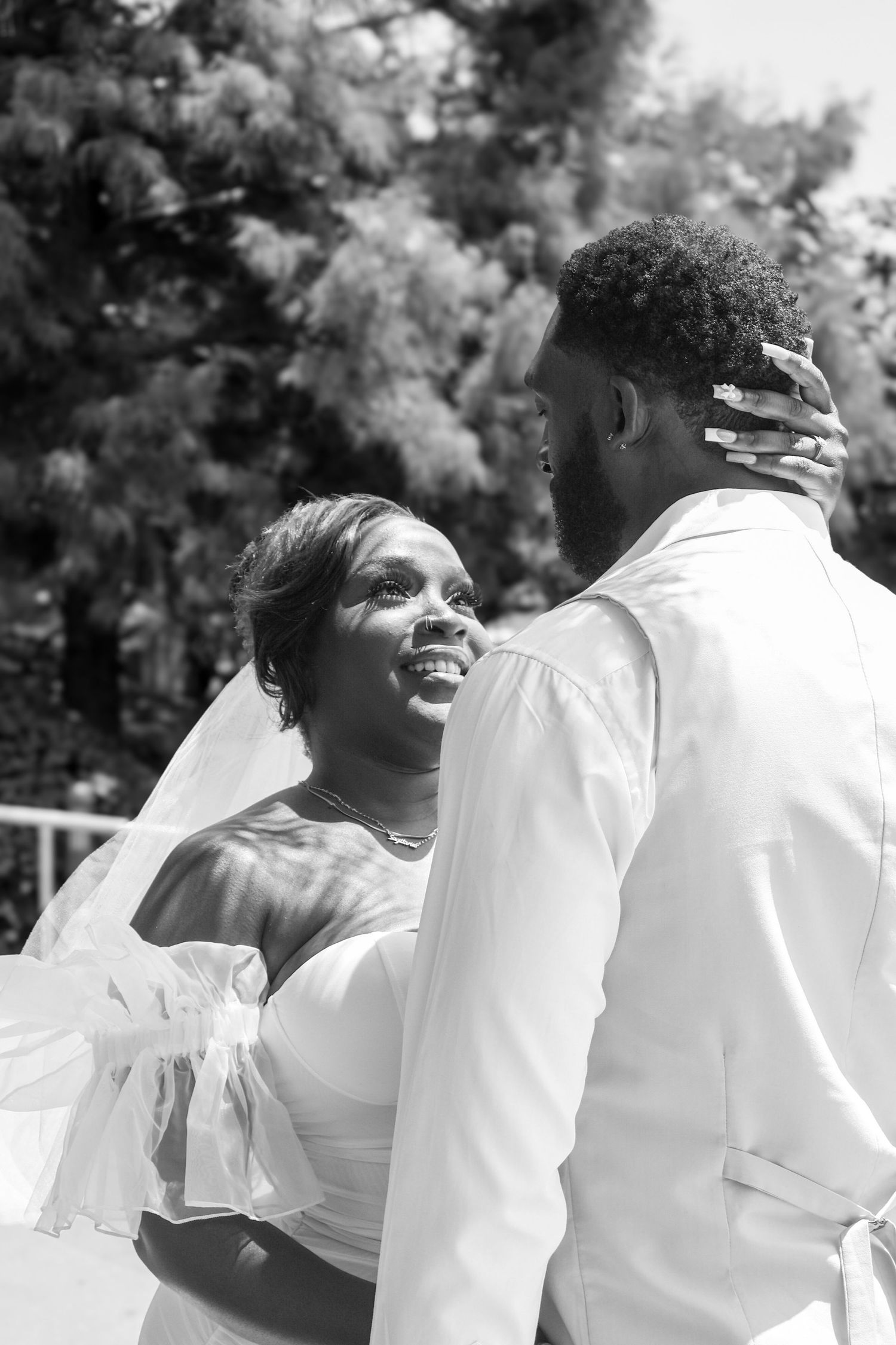 Black and white photo of joyful bride in veil embracing groom outdoors on wedding day.