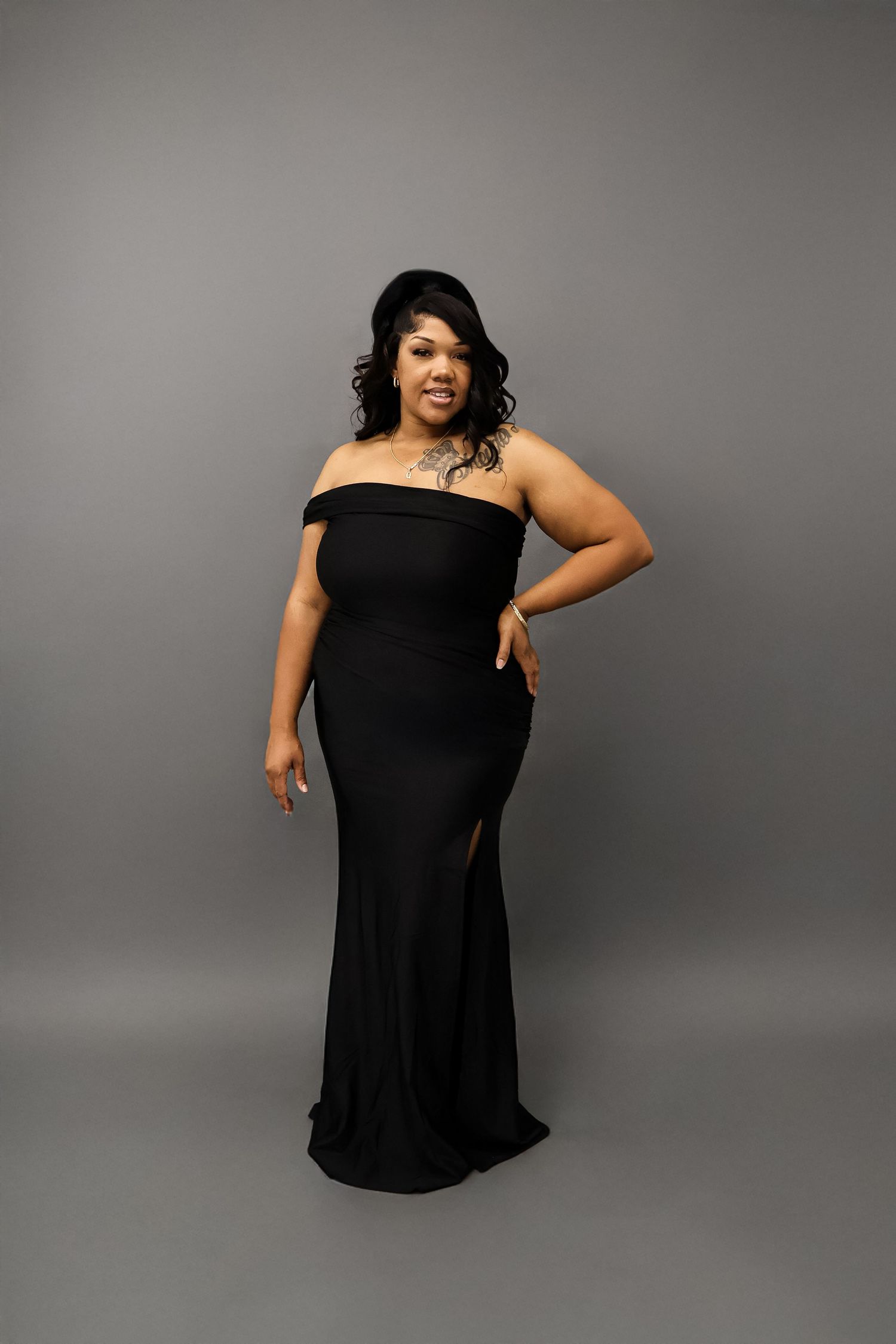 Woman in elegant off-shoulder black gown posing in studio setting.
