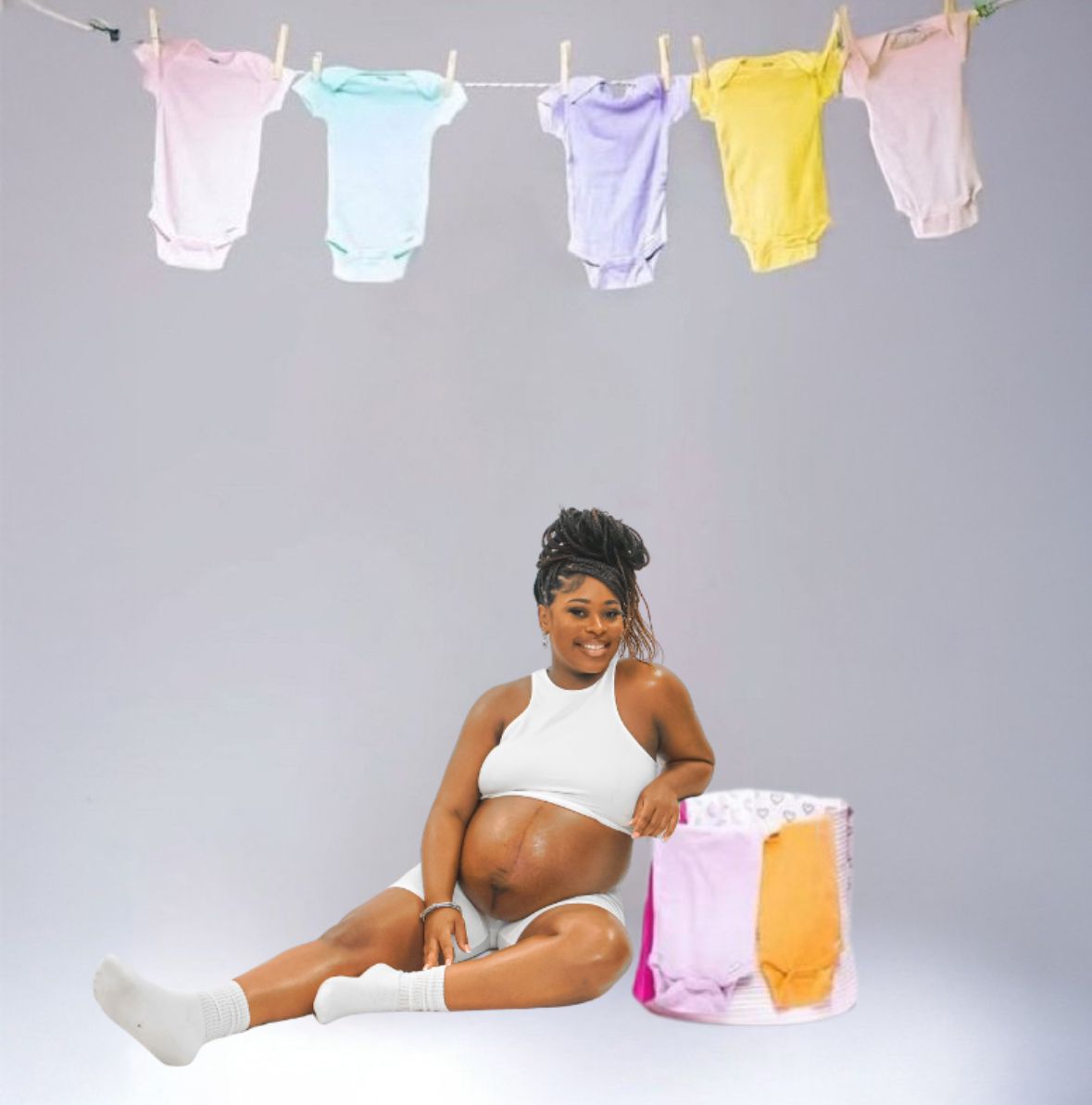 Pregnant woman sitting beside colorful baby clothes hanging on line above.