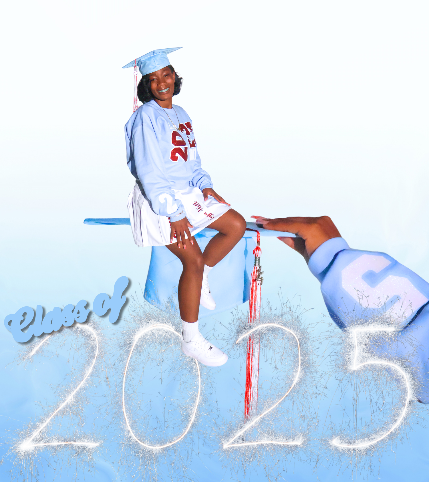 Class of 2025 graduate poses in light blue cap and sweatshirt with sparkle number design and tassel.
