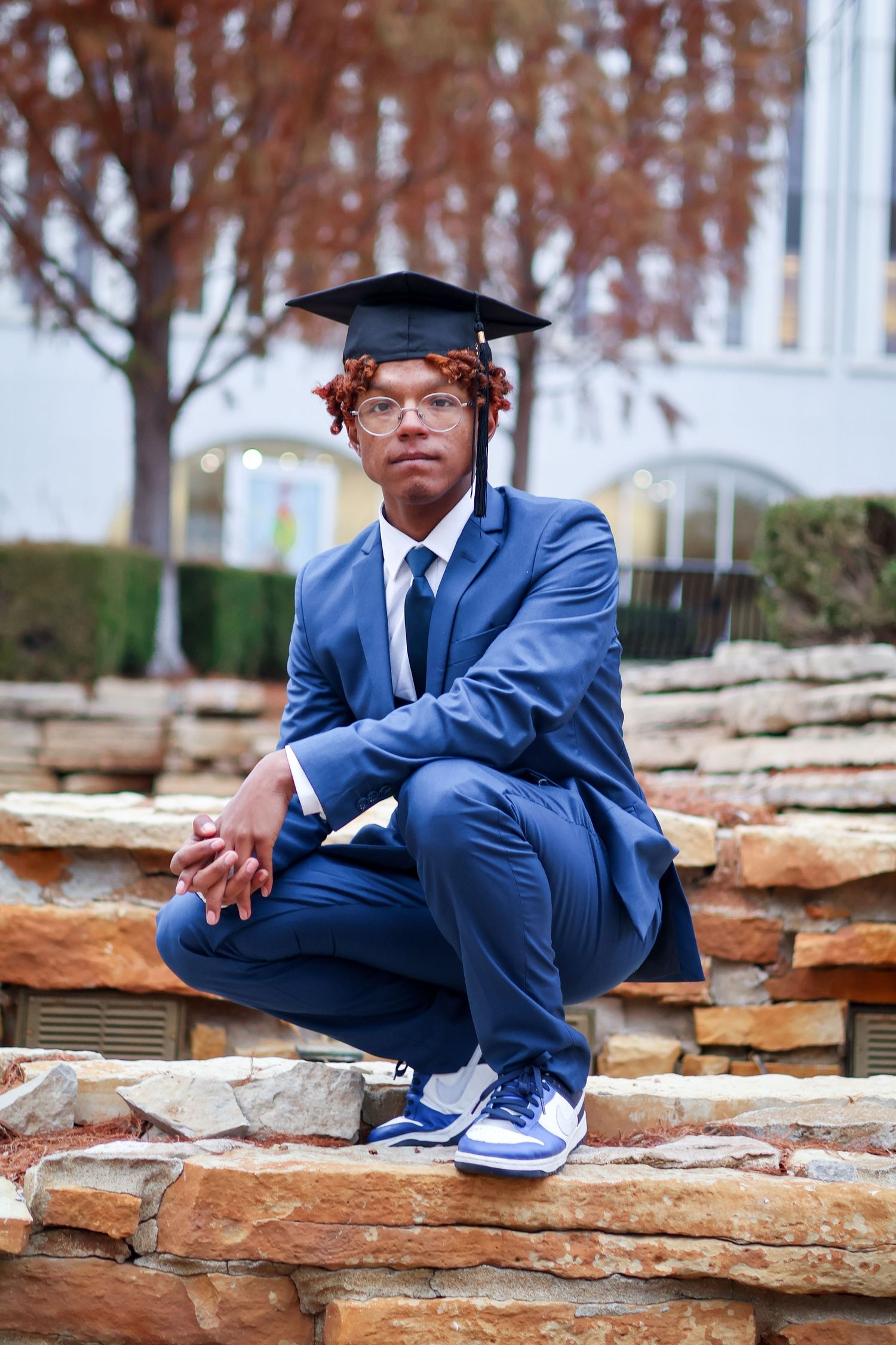 Young male graduate in blue suit and cap poses on stone steps outdoors.