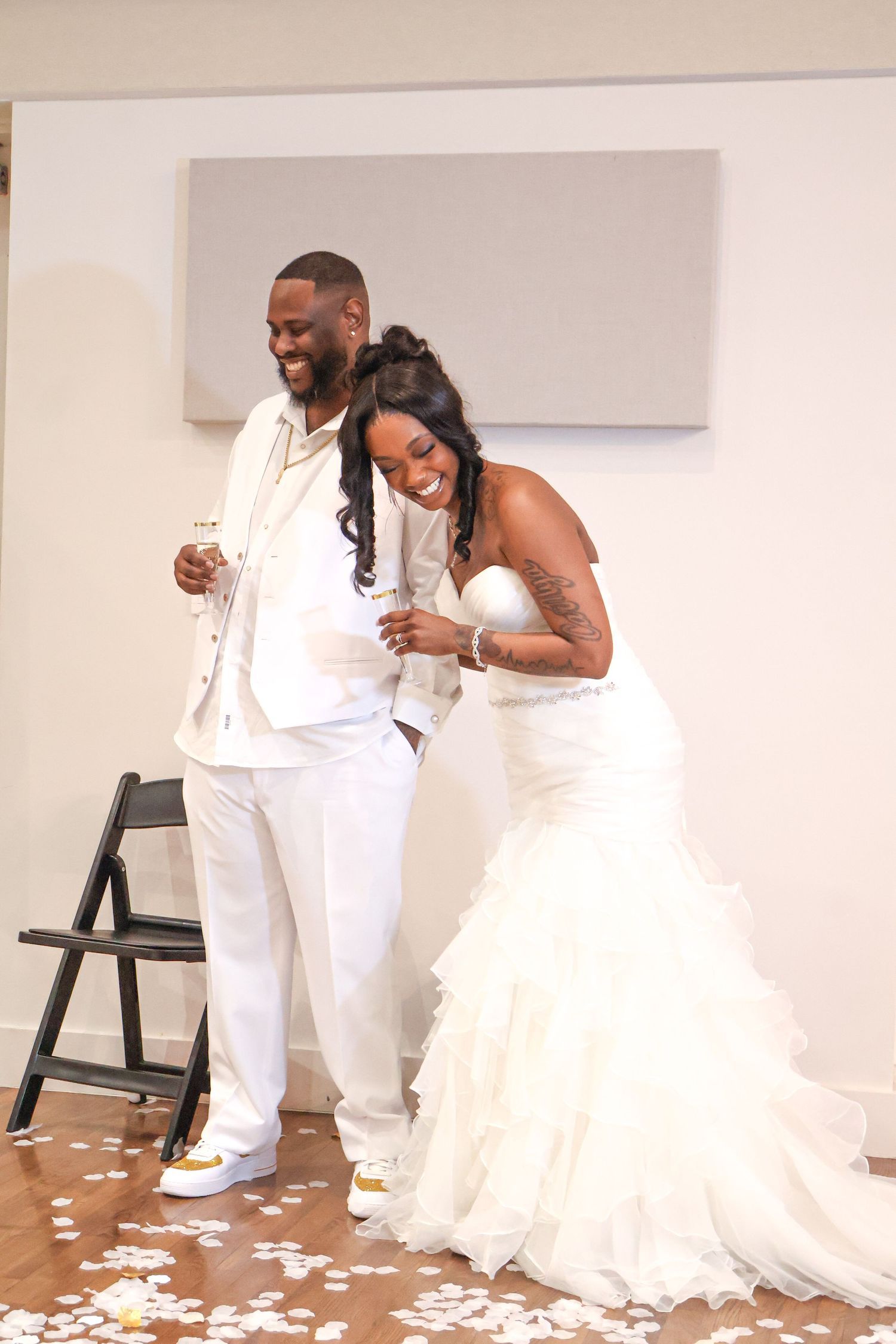 A joyful bride in a white mermaid gown and groom in a white suit celebrate their wedding reception.