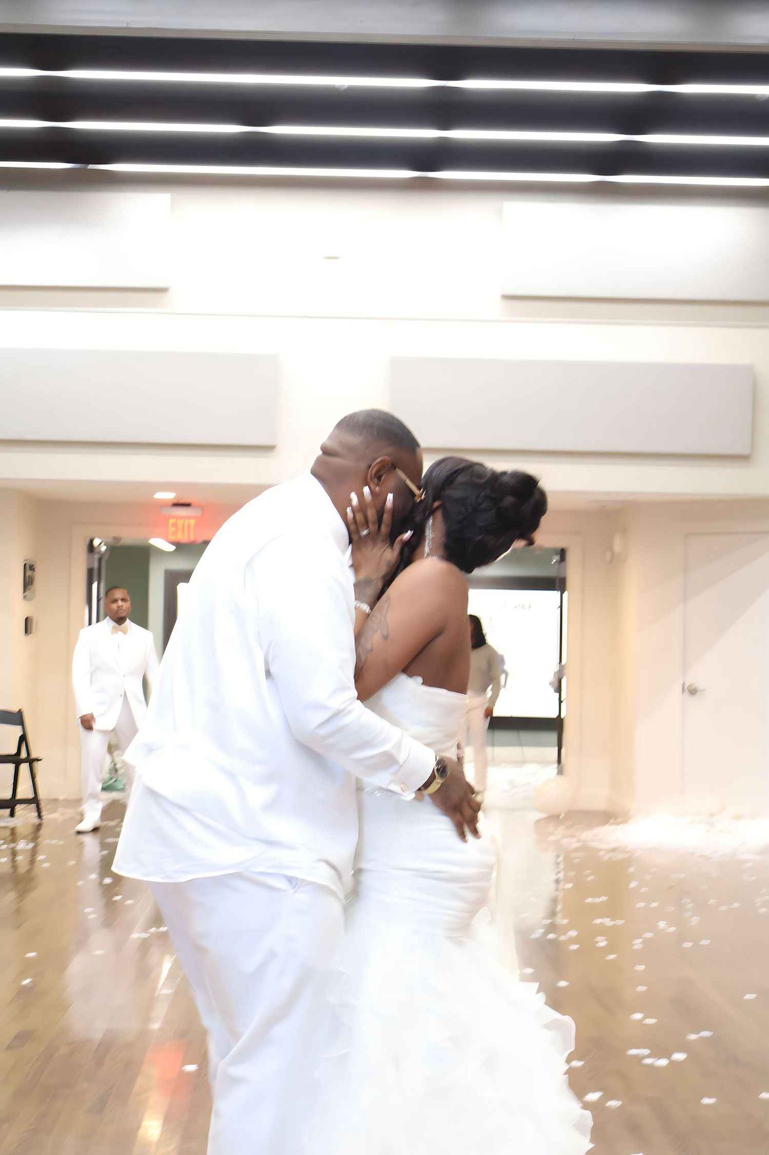 Bride and groom share a romantic first dance kiss in matching white wedding attire on dance floor.