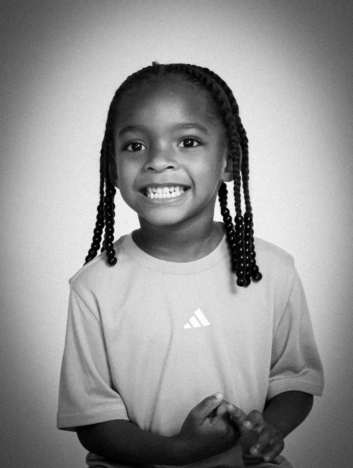 Smiling young child with braided hair wearing an Adidas t-shirt in a black and white portrait photo.