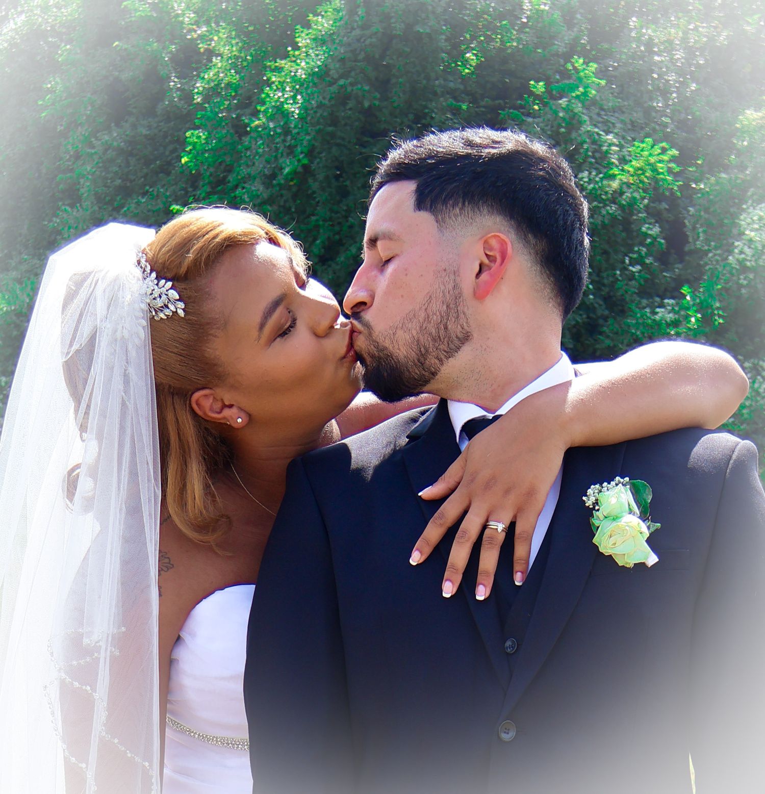 Bride and groom share romantic kiss outdoors surrounded by lush green trees on wedding day.