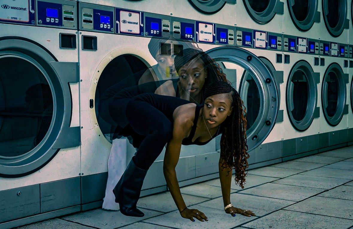 Two people pose dramatically in a laundromat with washing machines in a dark, artistic photo shoot.