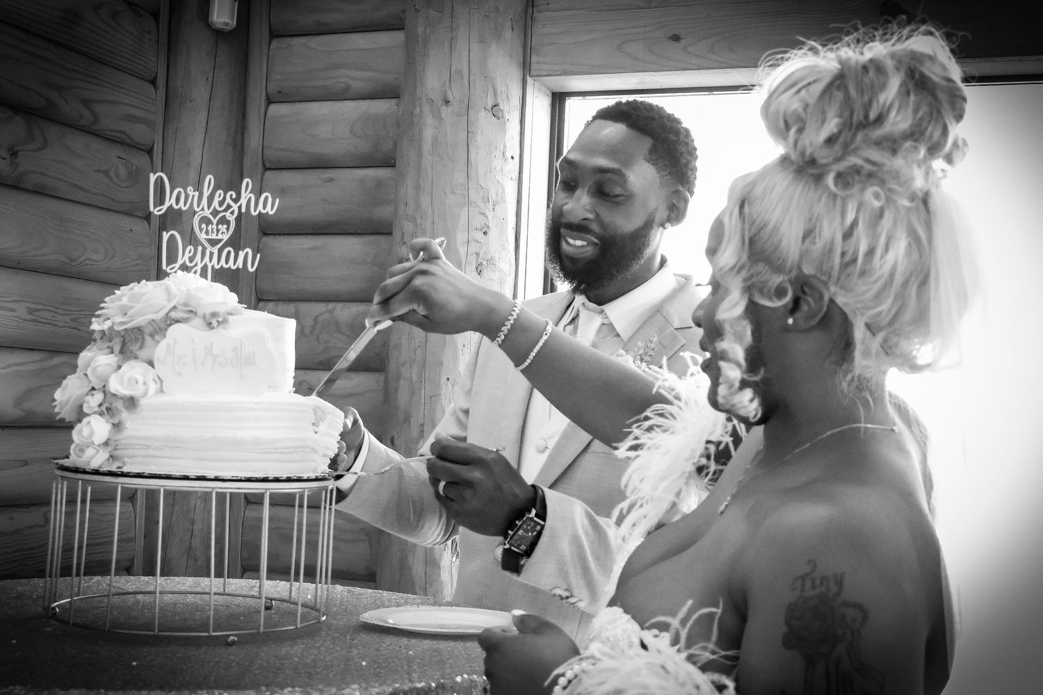 Bride and groom cutting their white wedding cake together in a black and white celebration photo.