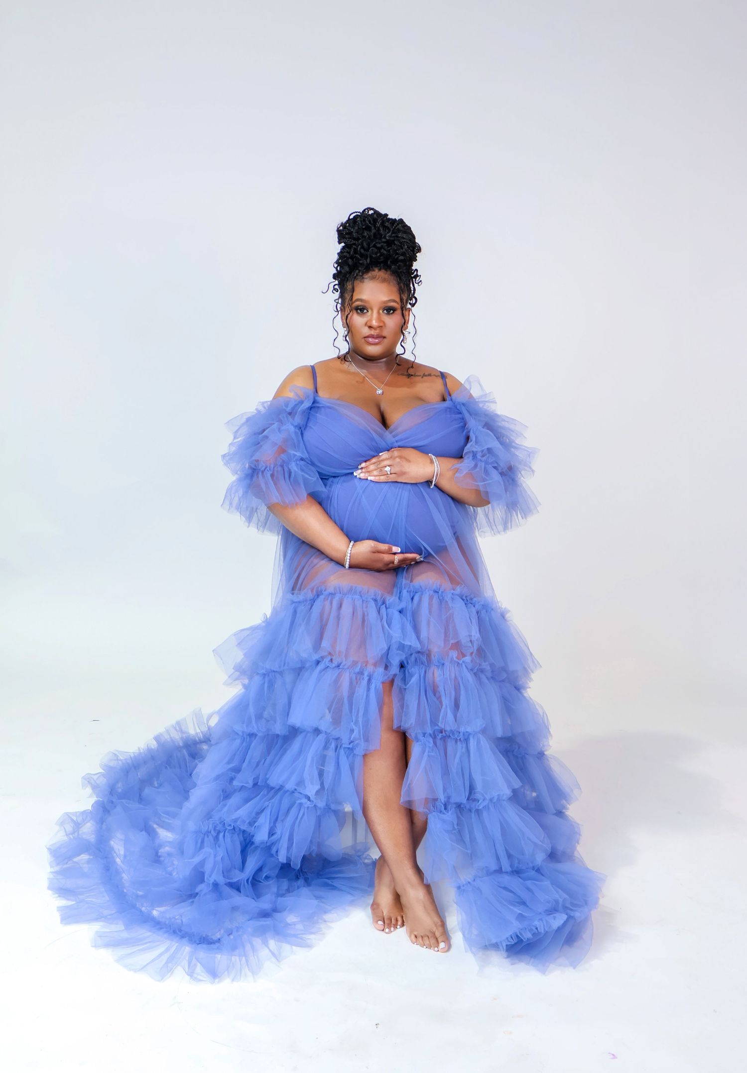 Pregnant woman in a blue ruffled tulle maternity gown posing for a professional maternity photoshoot.