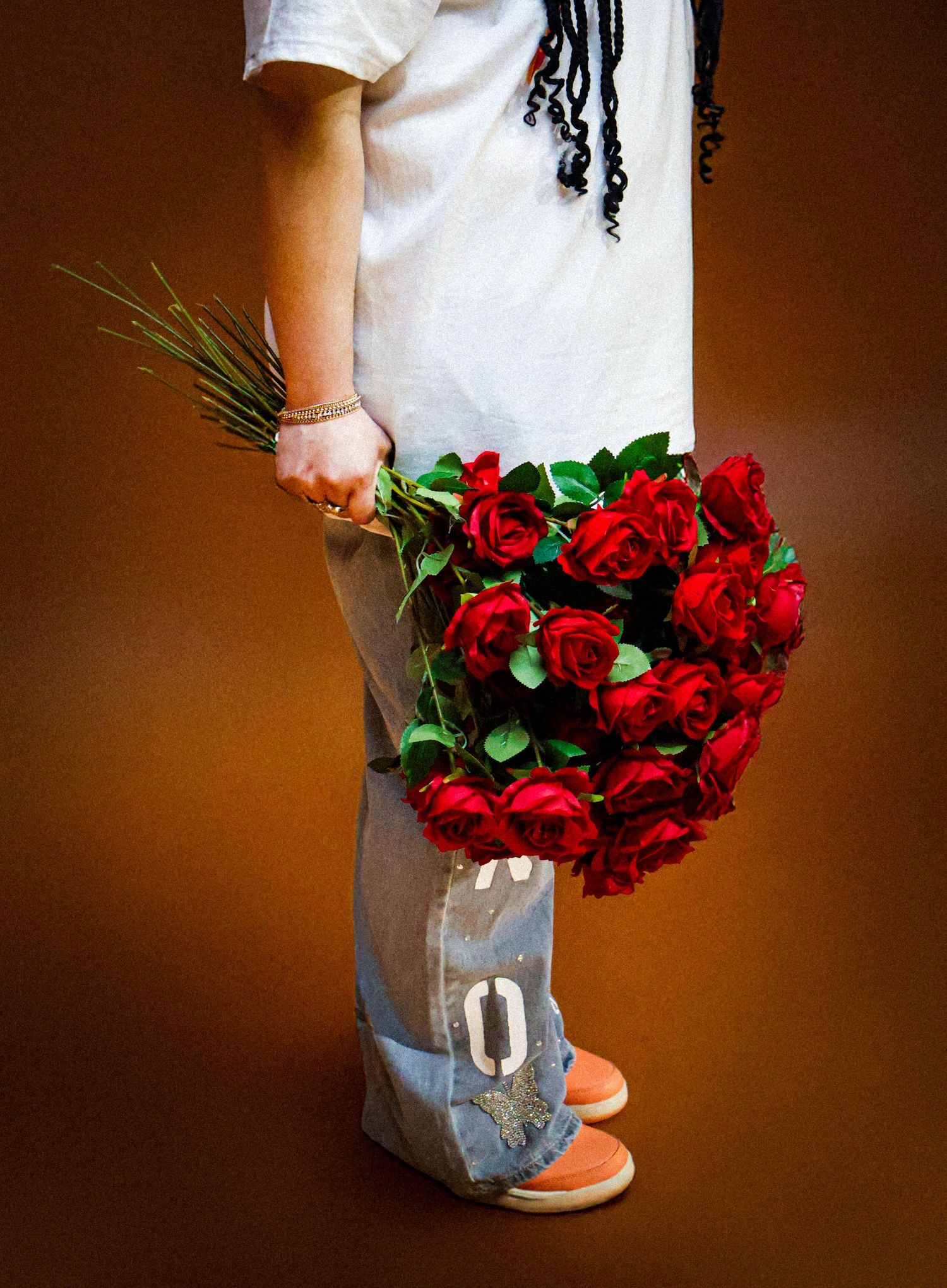 Person holding large bouquet of red roses with green stems against brown background.