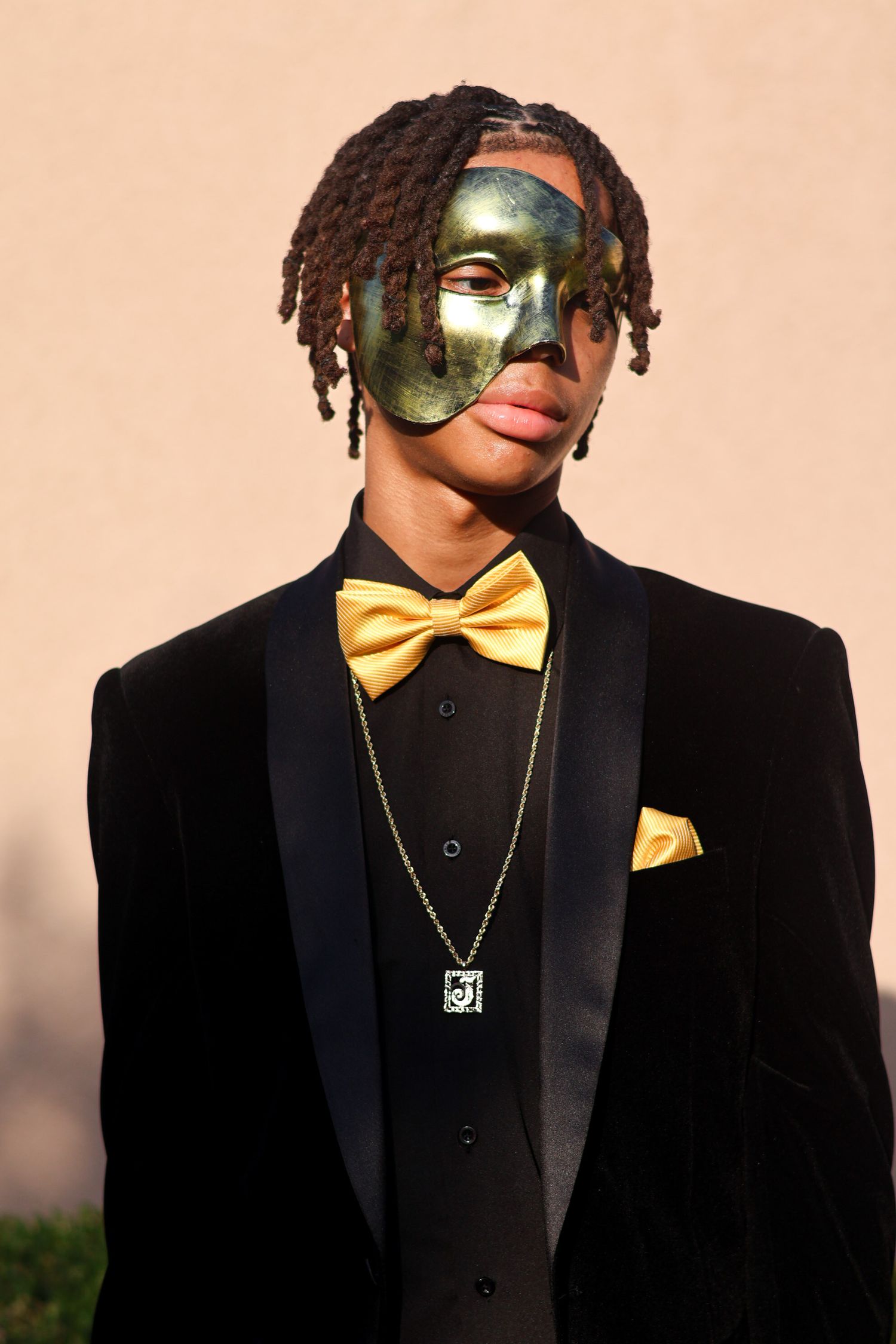Young man in black velvet suit with gold bow tie wearing decorative masquerade mask.