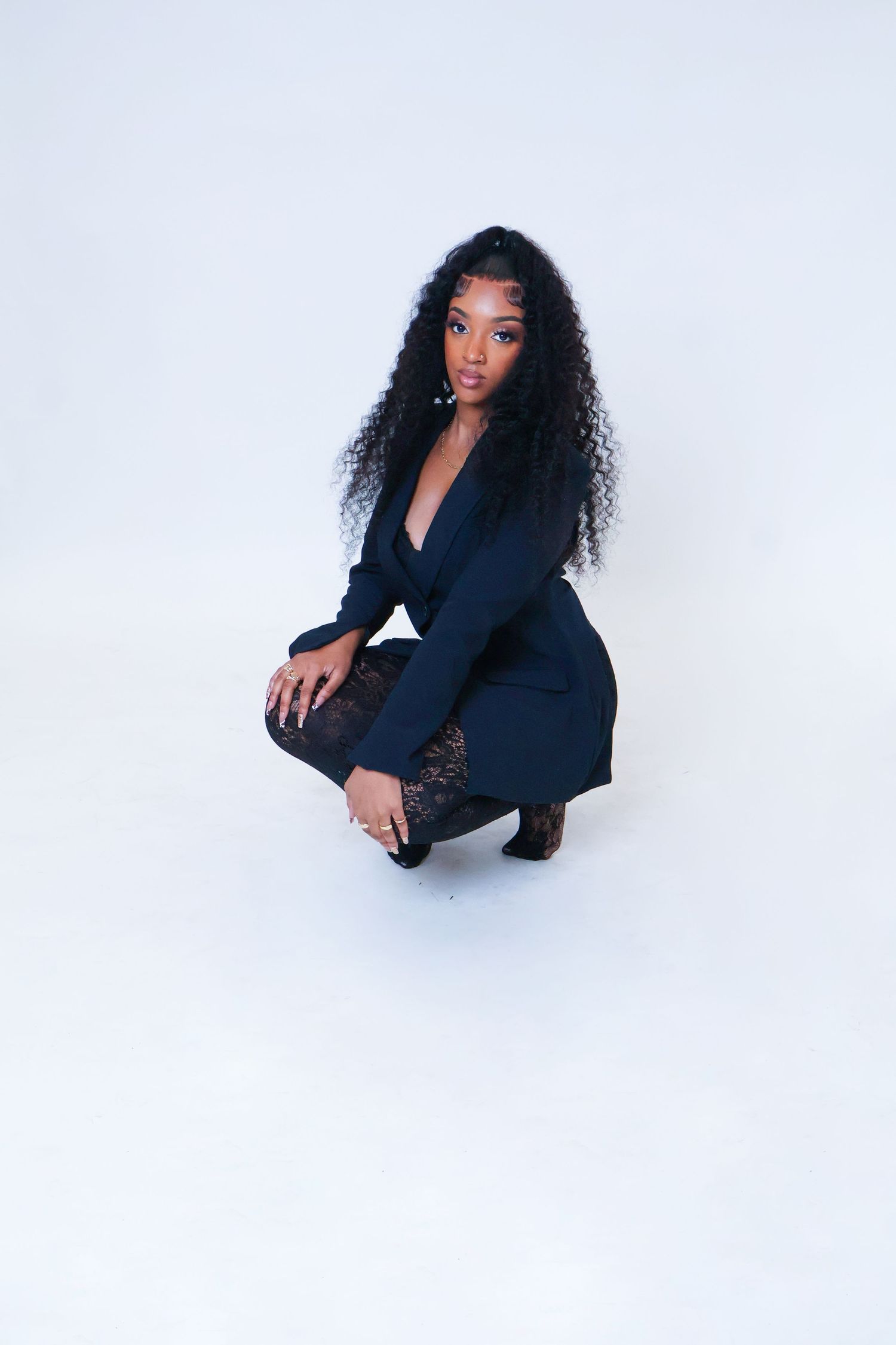 Woman with curly hair in navy blazer crouching on white floor.