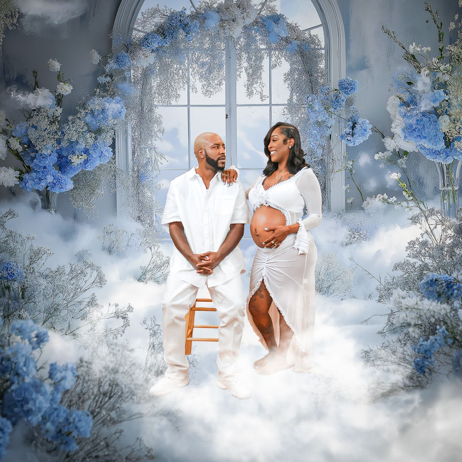 A couple in white poses for a maternity photo shoot surrounded by blue flowers and dreamy white clouds.