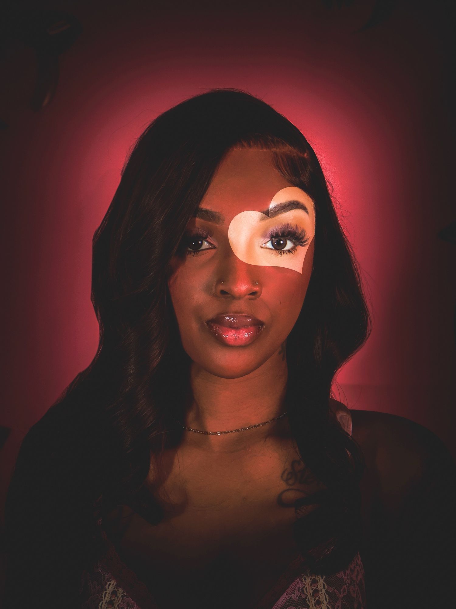 Portrait of woman with heart-shaped light projection on face against red background.