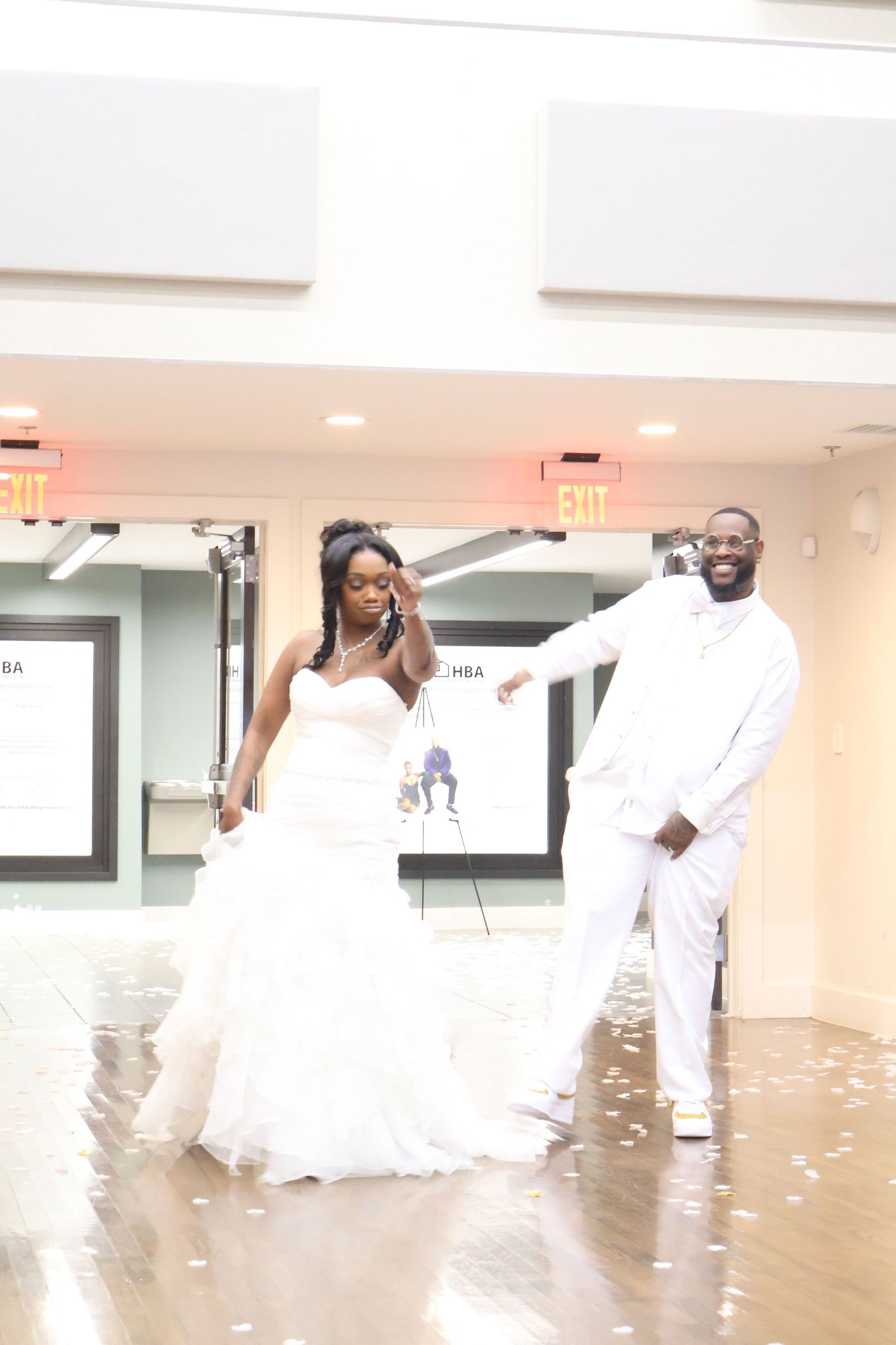 Bride and groom in white attire dancing at their wedding reception on a wooden dance floor.