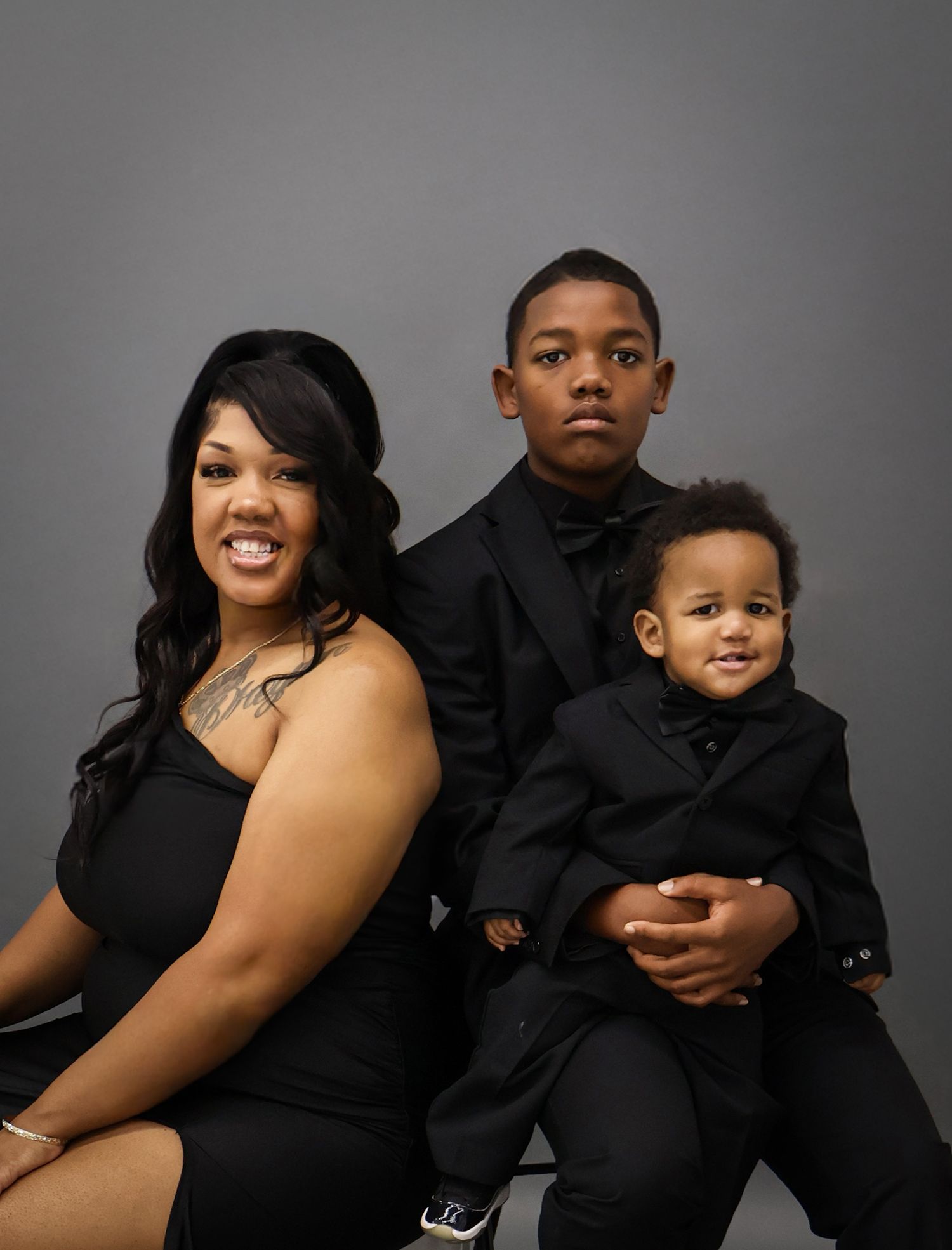 Woman in black dress posing with two boys in matching black suits.
