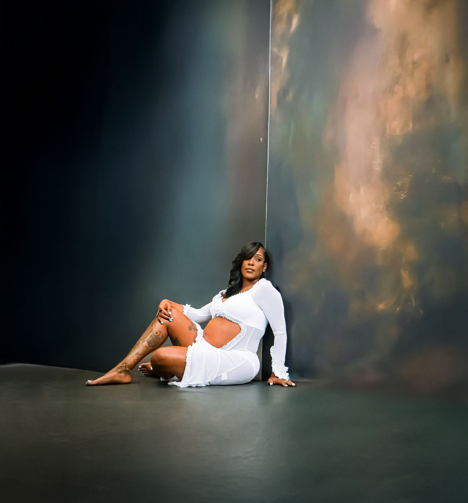 Woman in white cutout dress sitting gracefully on floor against dramatic stormy sky backdrop.