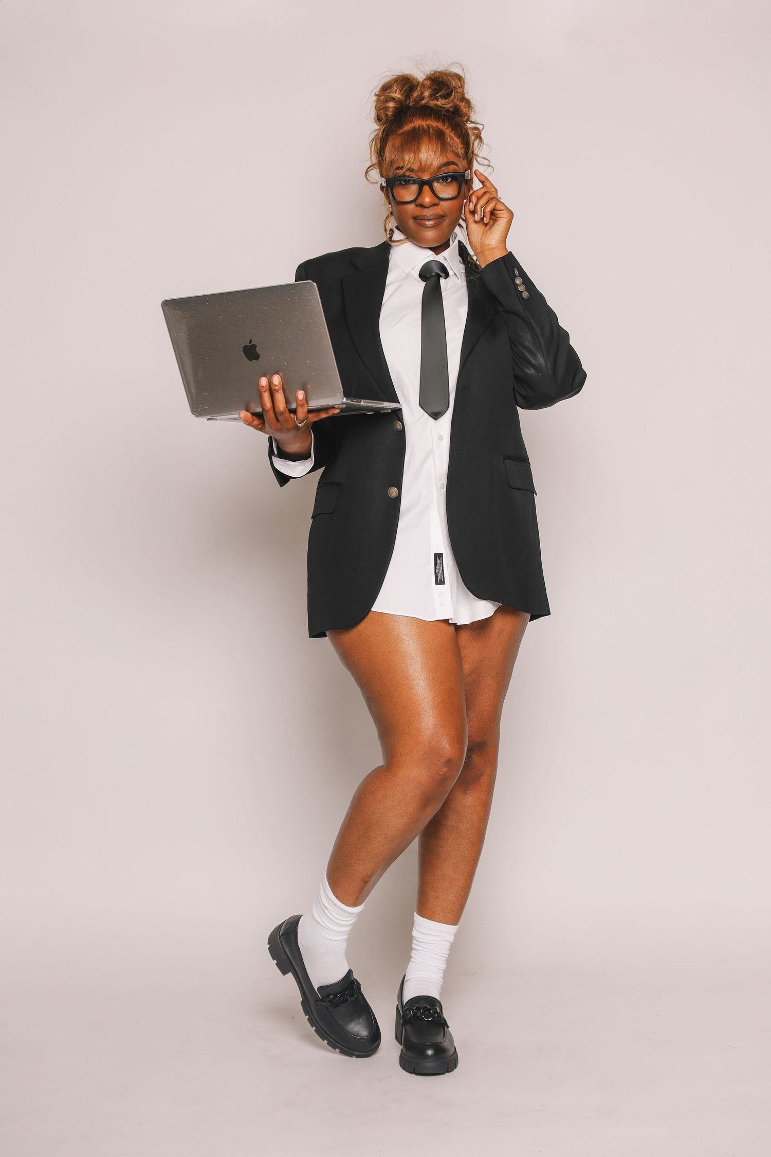 Woman in black blazer school uniform holding laptop while adjusting glasses on white background.