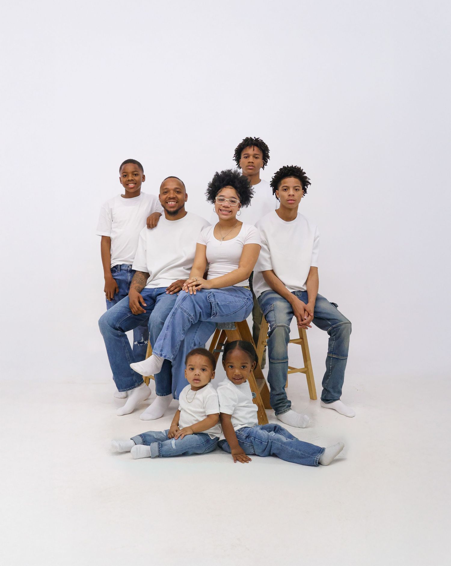 Family of six in matching white tees and jeans poses together in a bright studio portrait.