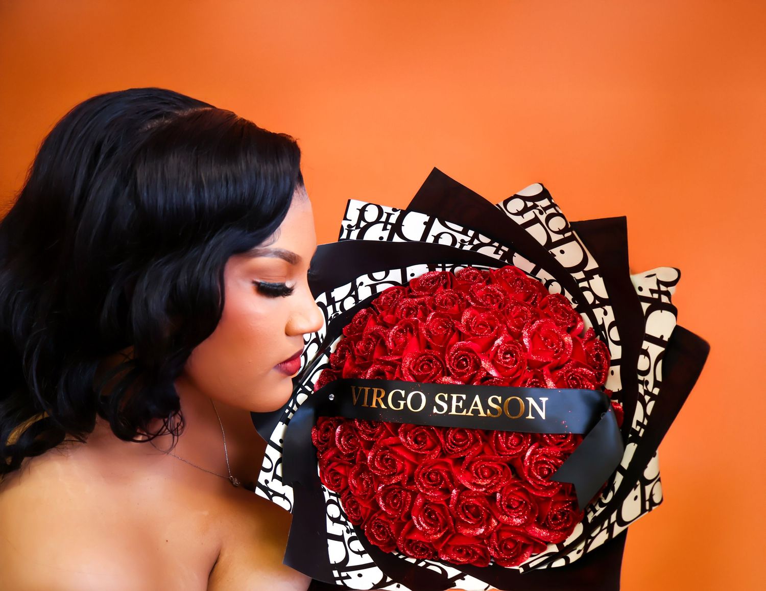 Young woman with wavy hair holding large bouquet of red roses labeled Virgo Season on orange background.