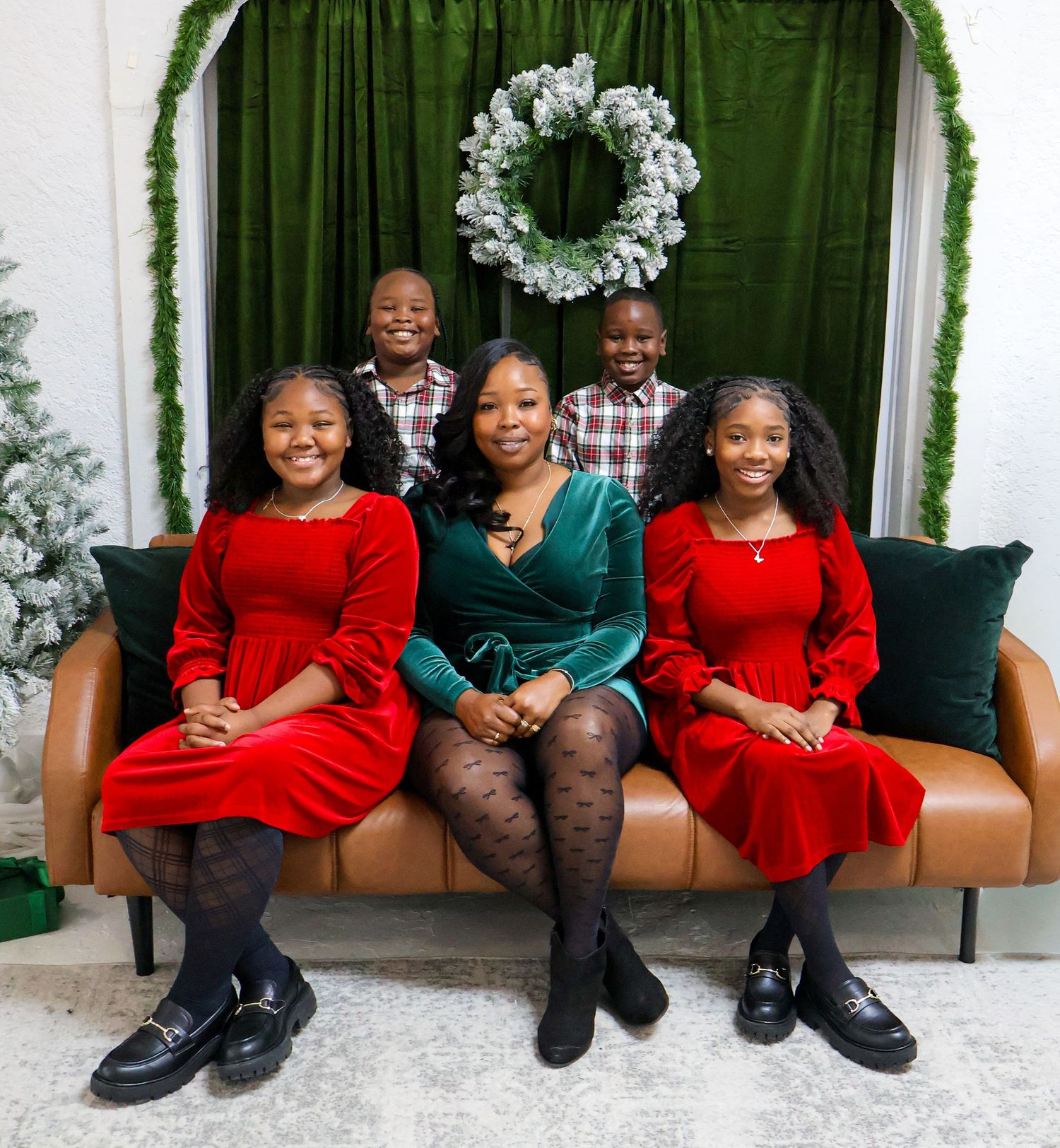 Family Christmas portrait with mother and four children in red and green velvet outfits on sofa.