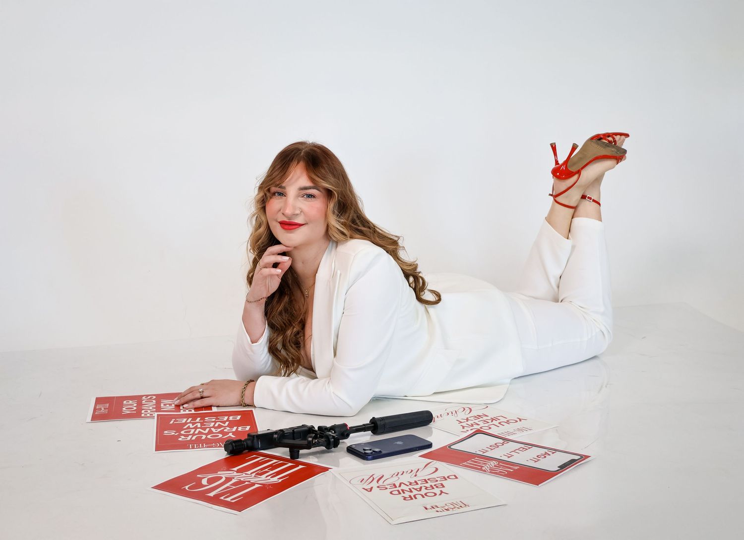 Woman in white outfit poses with red marketing cards and hair tools on white background.