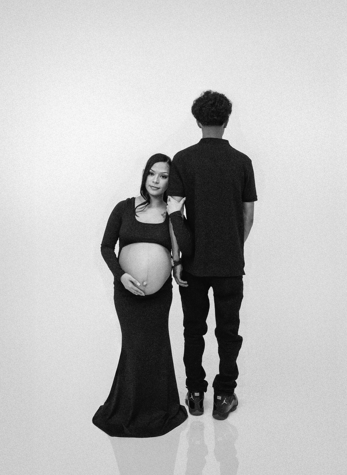 Black and white maternity photo of couple in black outfits, woman cradling baby bump.