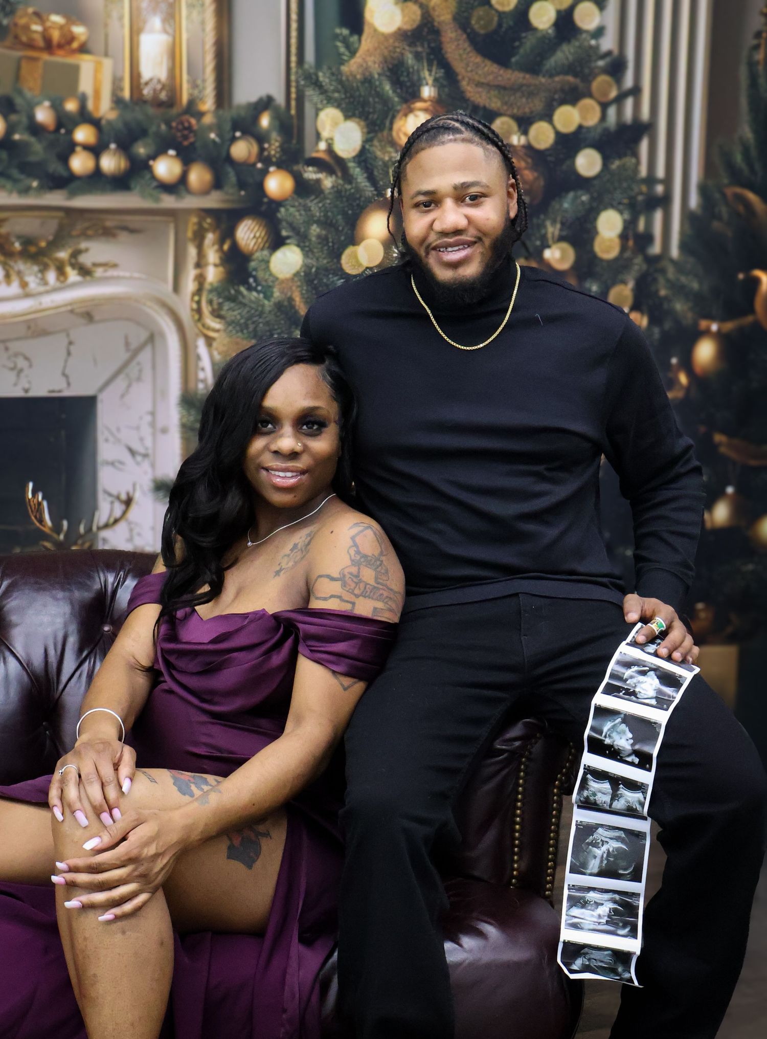 A couple poses for a Christmas maternity photo, holding ultrasound images, with a decorated tree in the background.