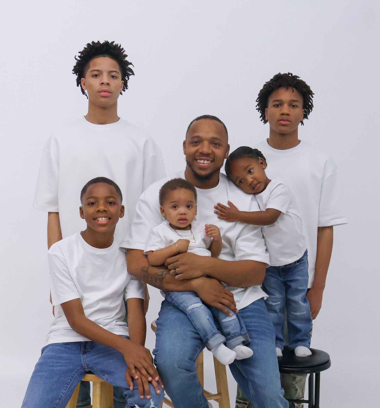 A man poses with four boys in matching white shirts and jeans for a professional family portrait.