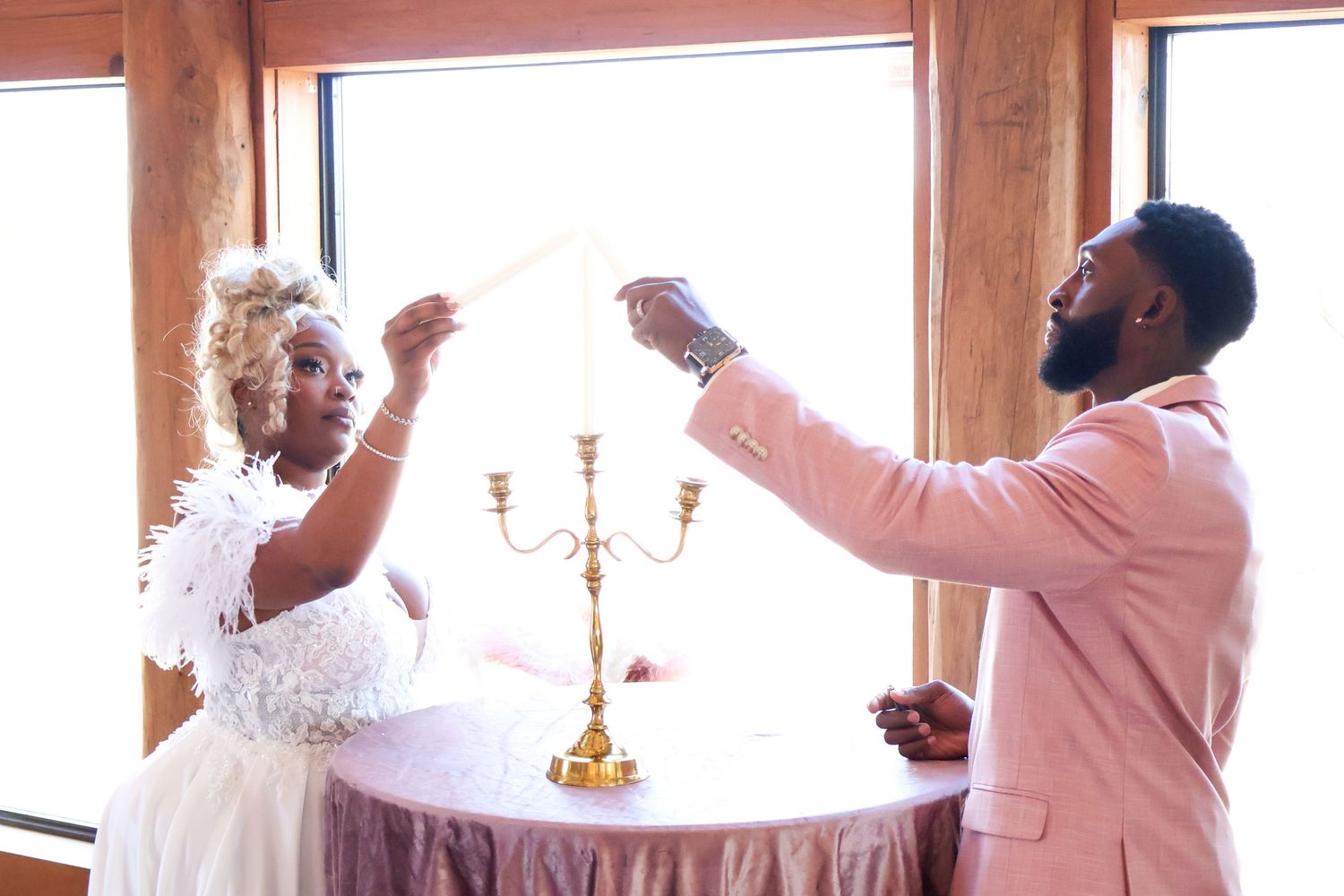 Older couple lighting unity candle with gold candelabra at intimate indoor wedding ceremony.