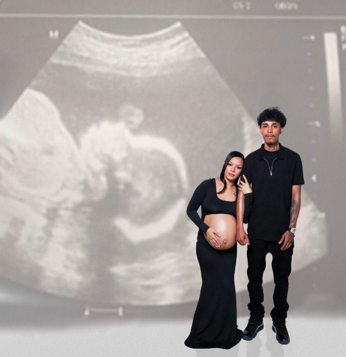 Pregnant couple in matching black outfits posing in front of an ultrasound image backdrop.