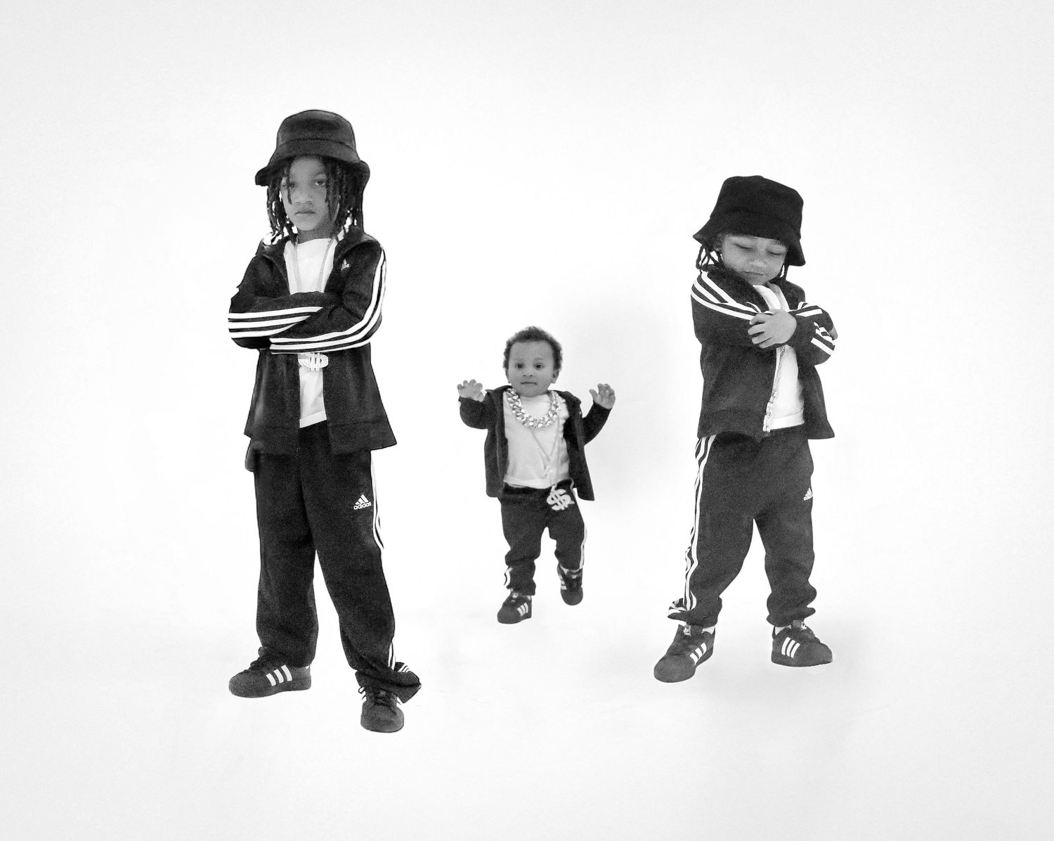 Black and white photo of three children in matching Adidas tracksuits posing together.