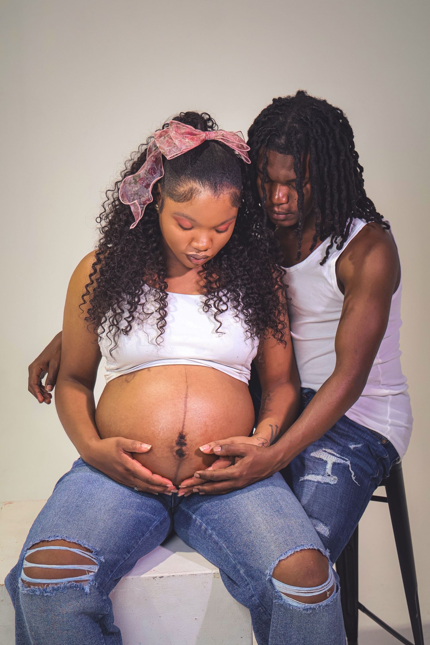 A pregnant woman and her partner tenderly cradle her baby bump during a maternity photo shoot.