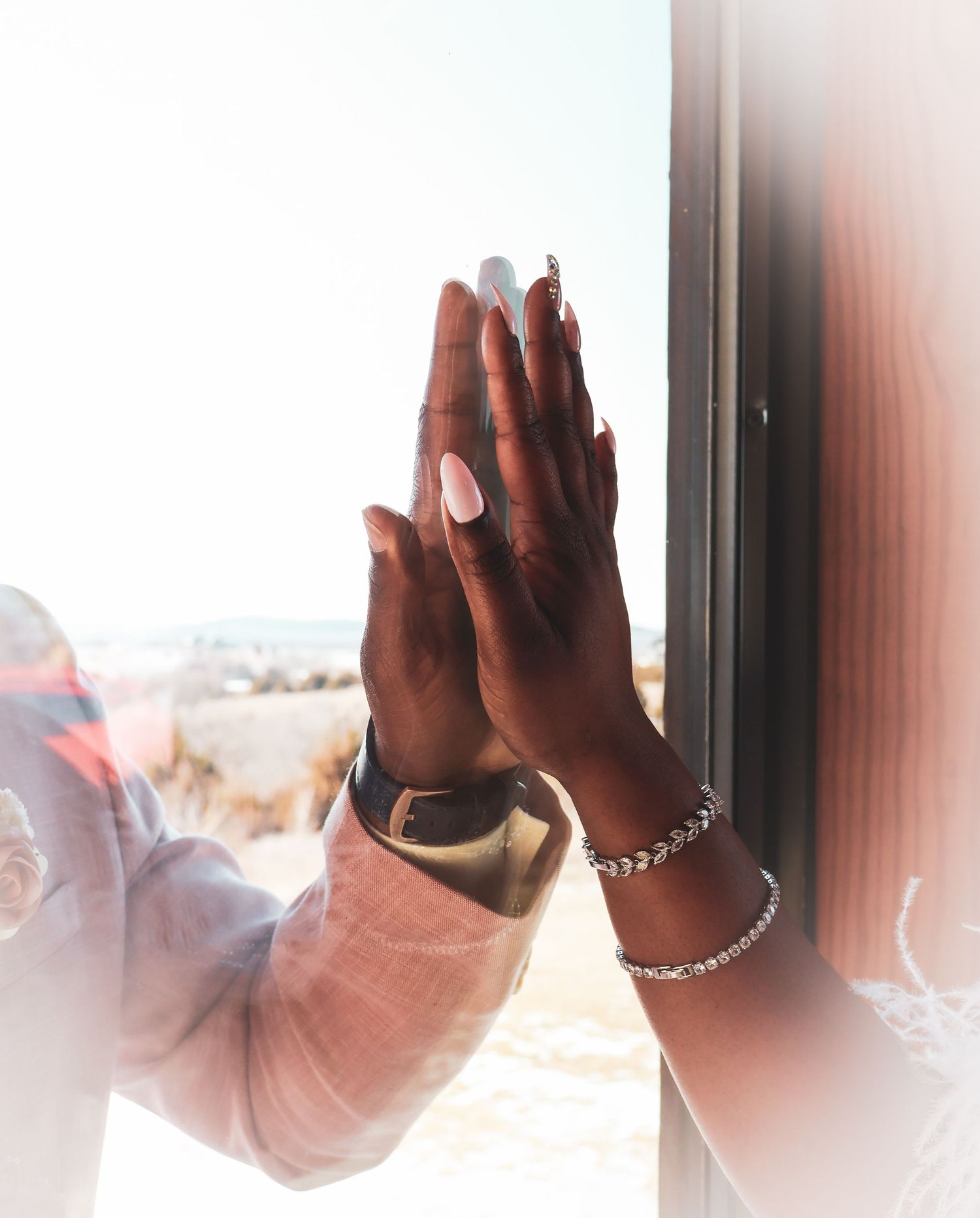 Two hands pressed together near a sunlit window with a silver bracelet and manicured nails.