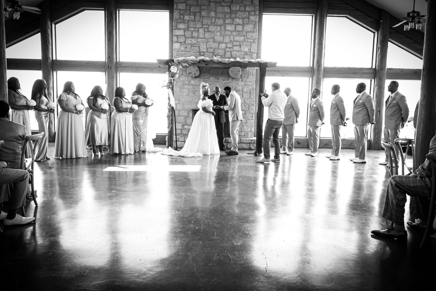 Black and white photo of wedding ceremony with bridal party at stone fireplace altar.