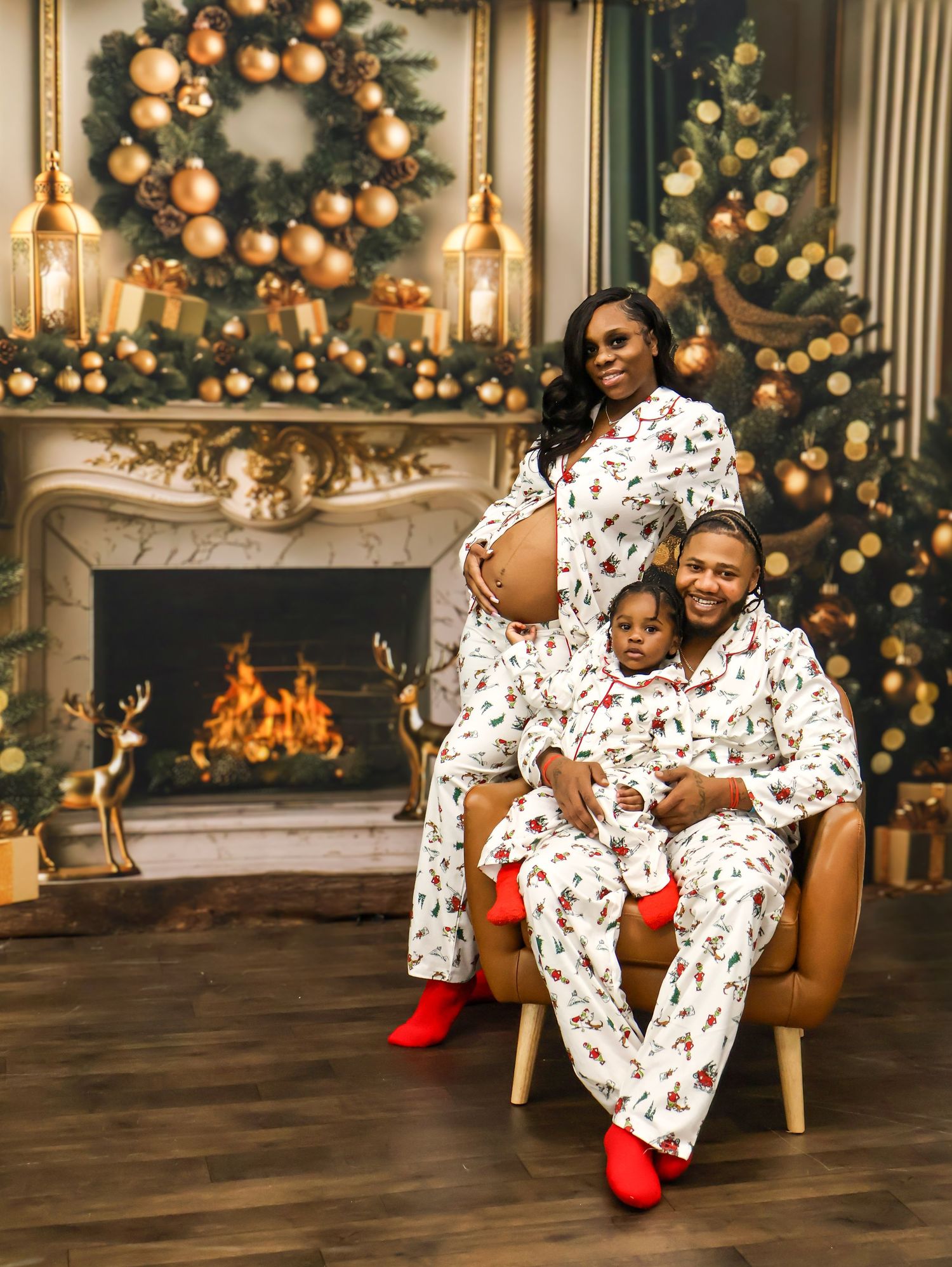 Family in matching Christmas pajamas posing by a decorated fireplace, with a pregnant mother, father, and young child.